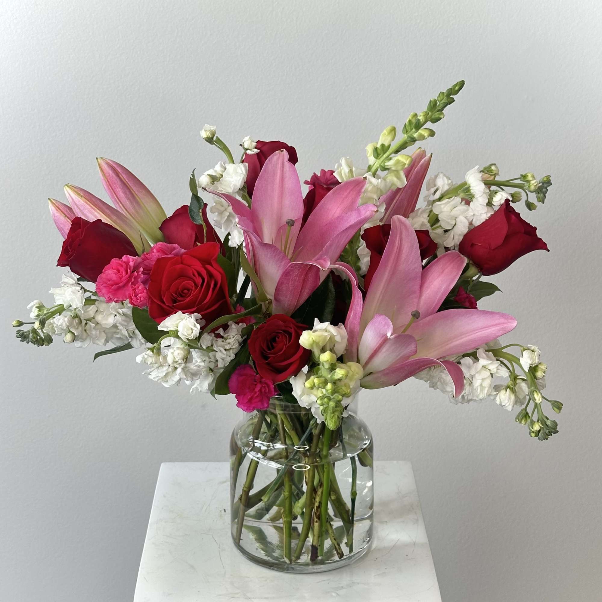 Pink lilies and red roses arranged in a clear glass vase