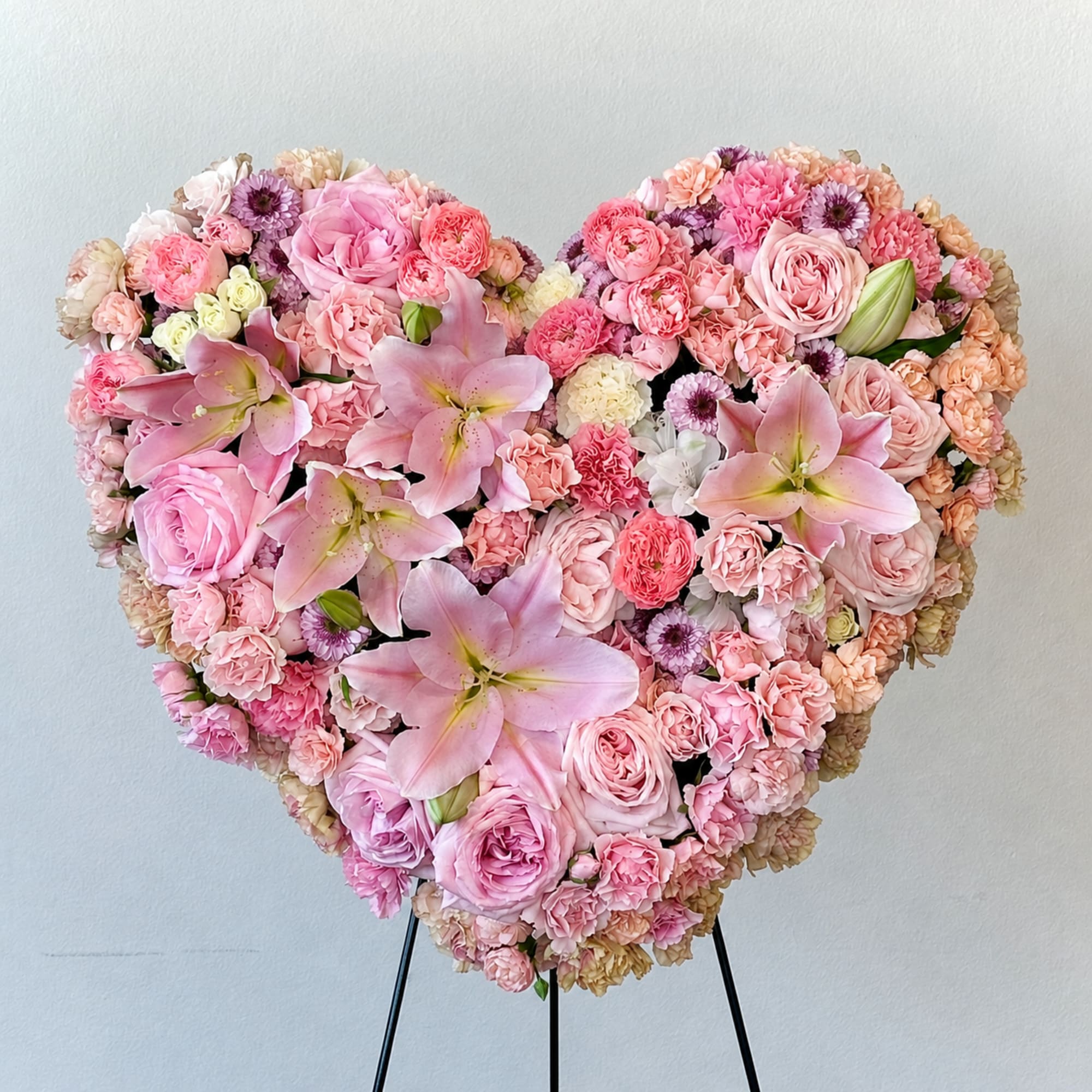 Heart-shaped arrangement of pink roses, lilies, and carnations on a stand