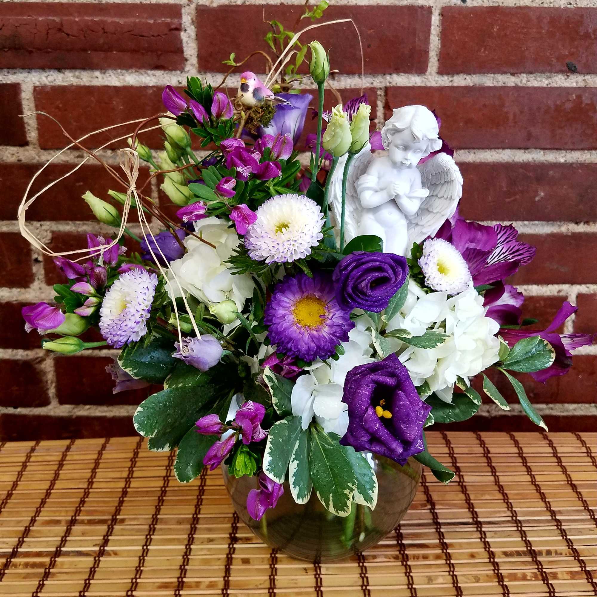 Purple and white floral arrangement in a glass vase with a small angel figurine