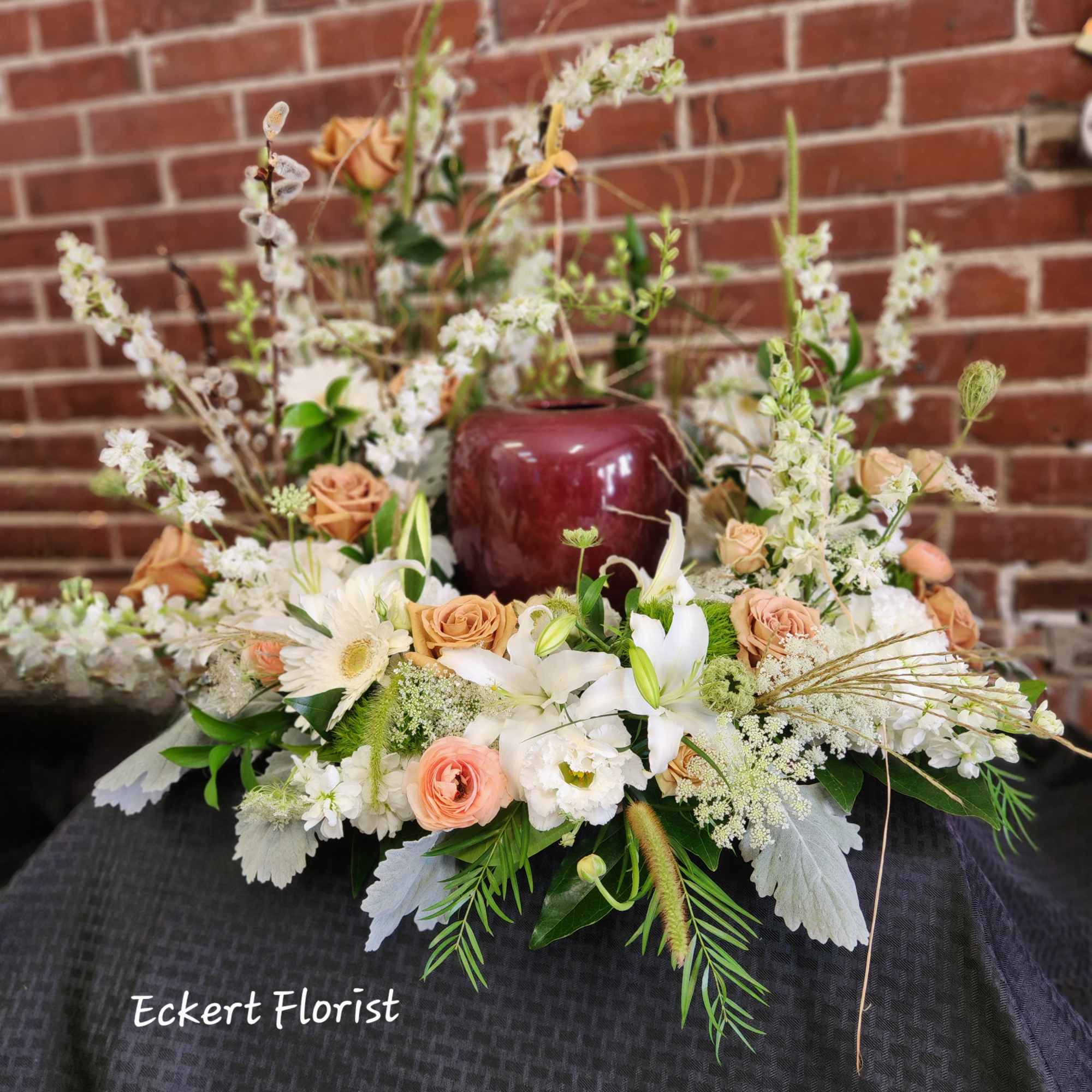 Low floral arrangement with white lilies, peach roses, and white daisies in a burgundy vase
