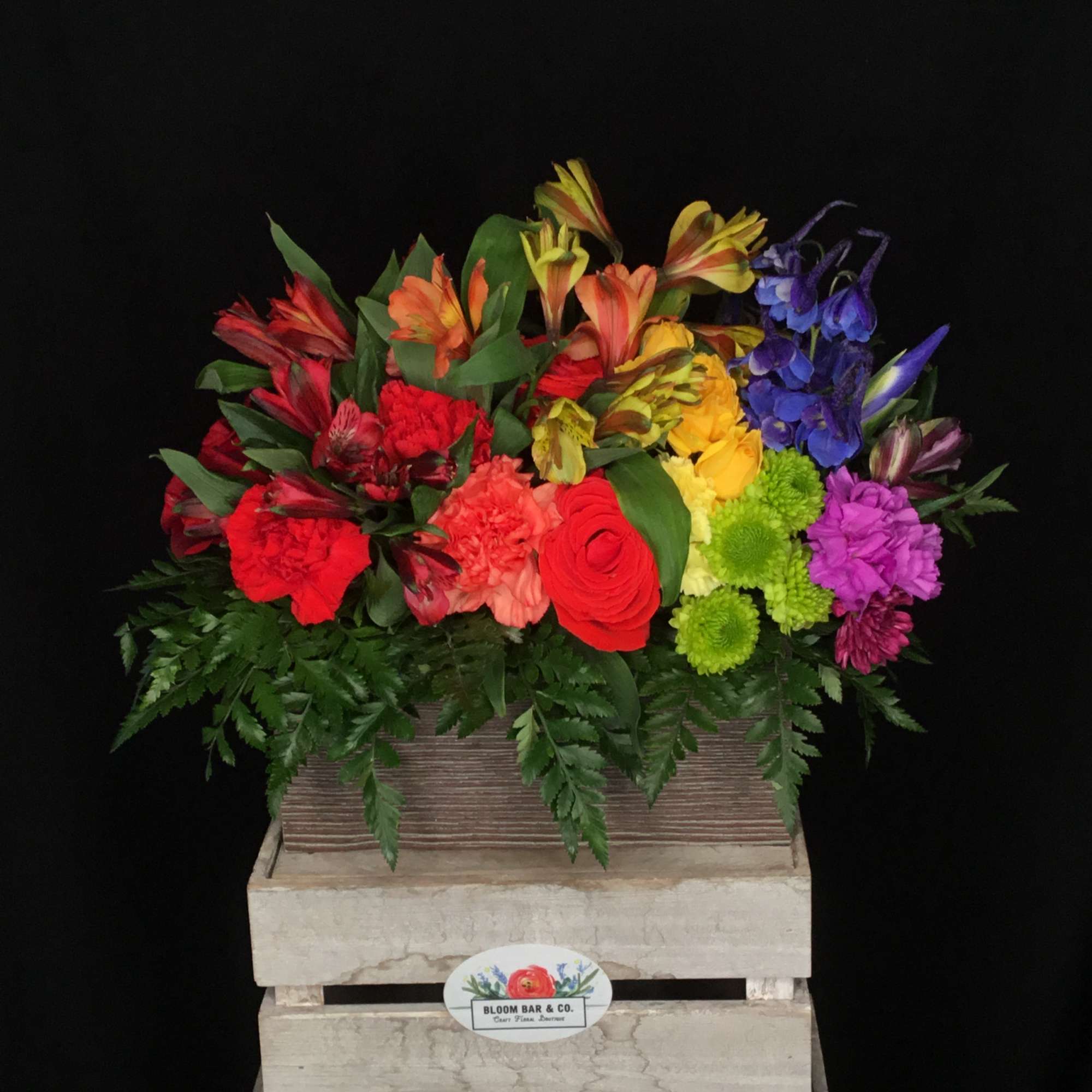 Bright mixed bouquet in a wooden crate with red, yellow, purple, and orange blooms