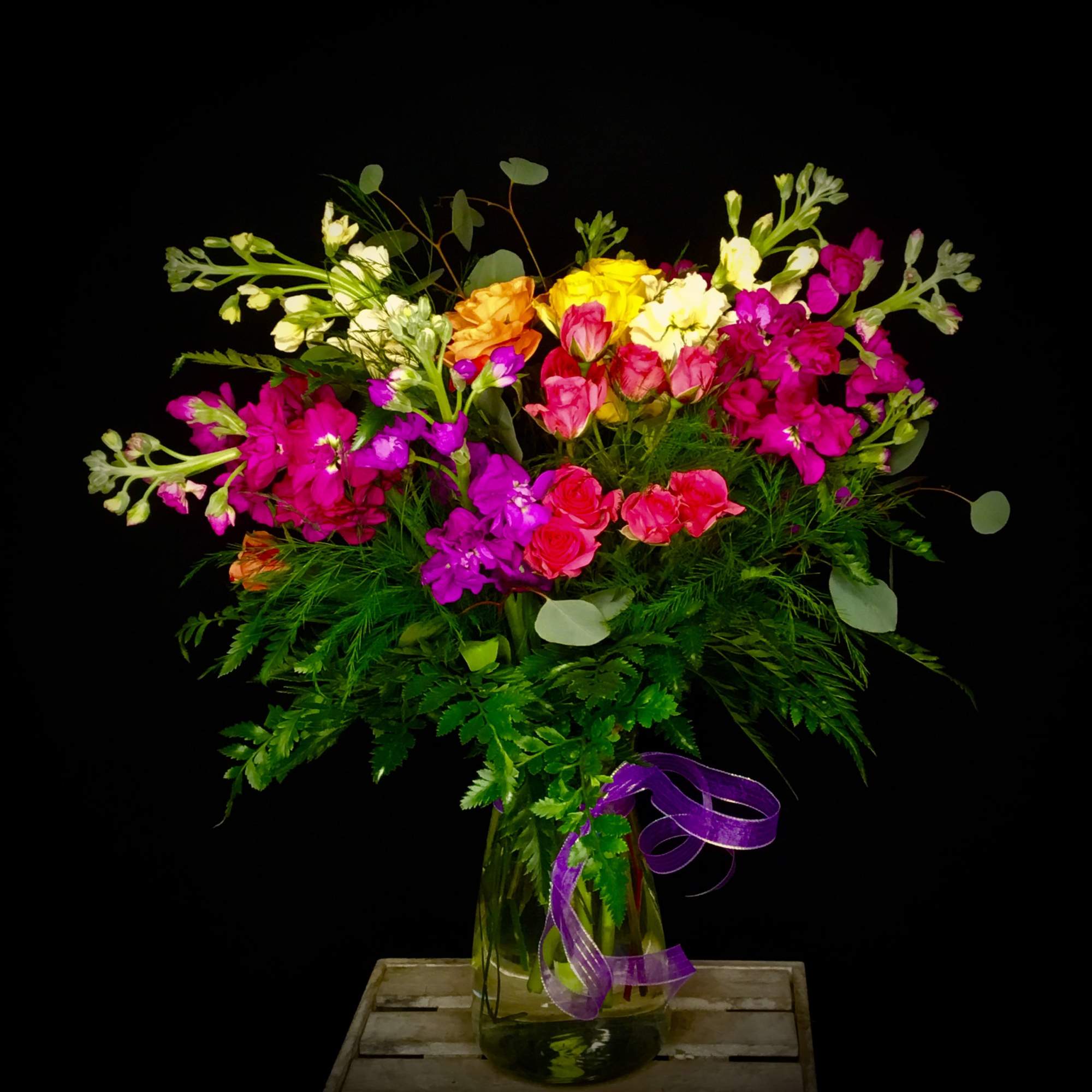 Colorful mixed bouquet in a glass vase with a purple ribbon