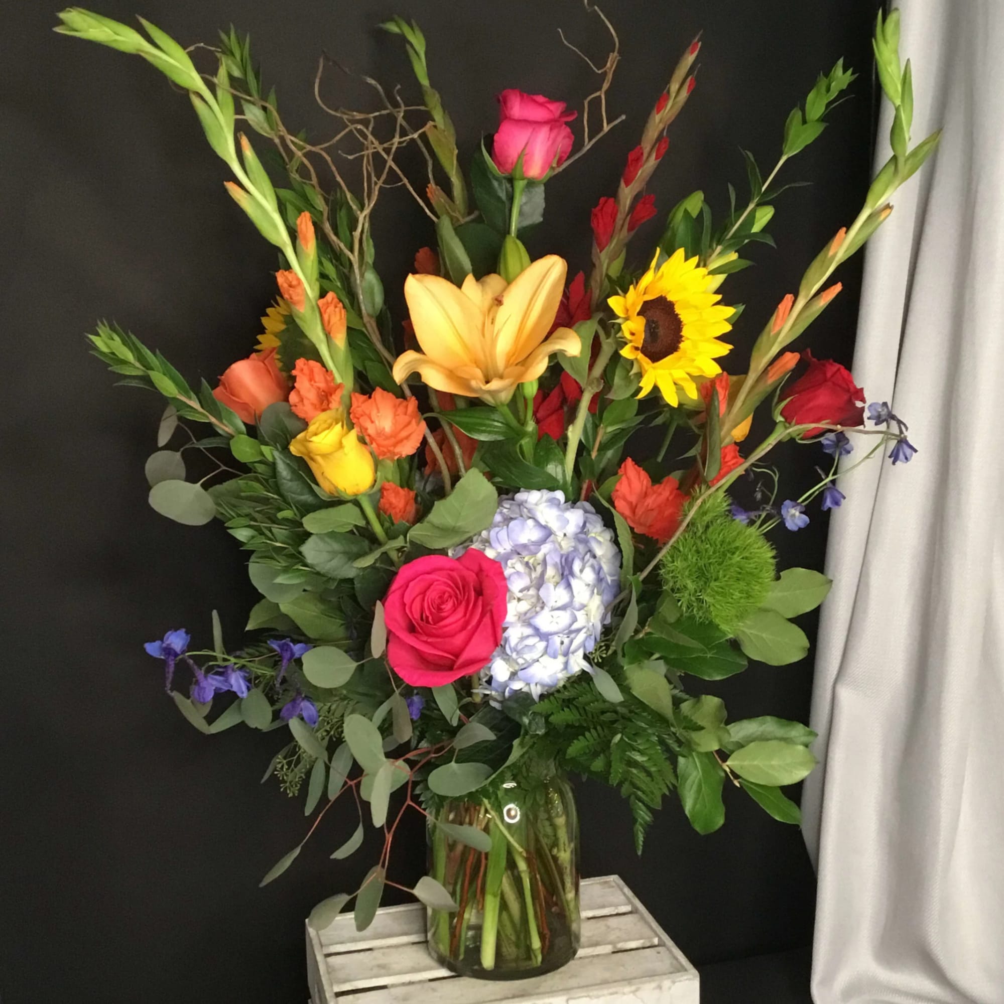 Tall mixed bouquet with roses, lilies, sunflower, and hydrangea in a glass vase
