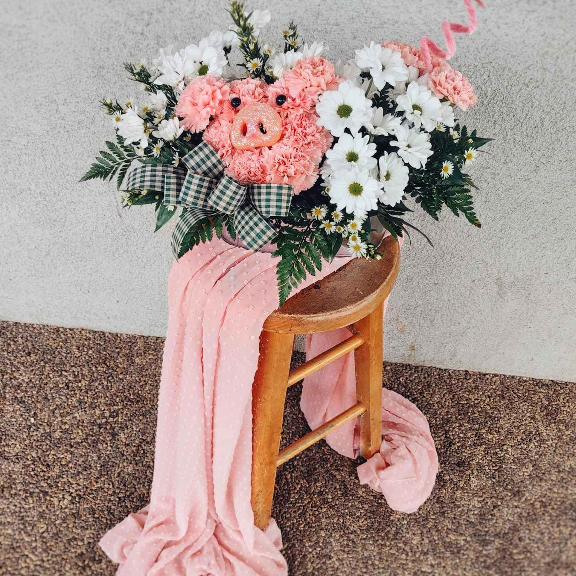 Pink pig-shaped floral arrangement with white daisies and a plaid bow on a stool