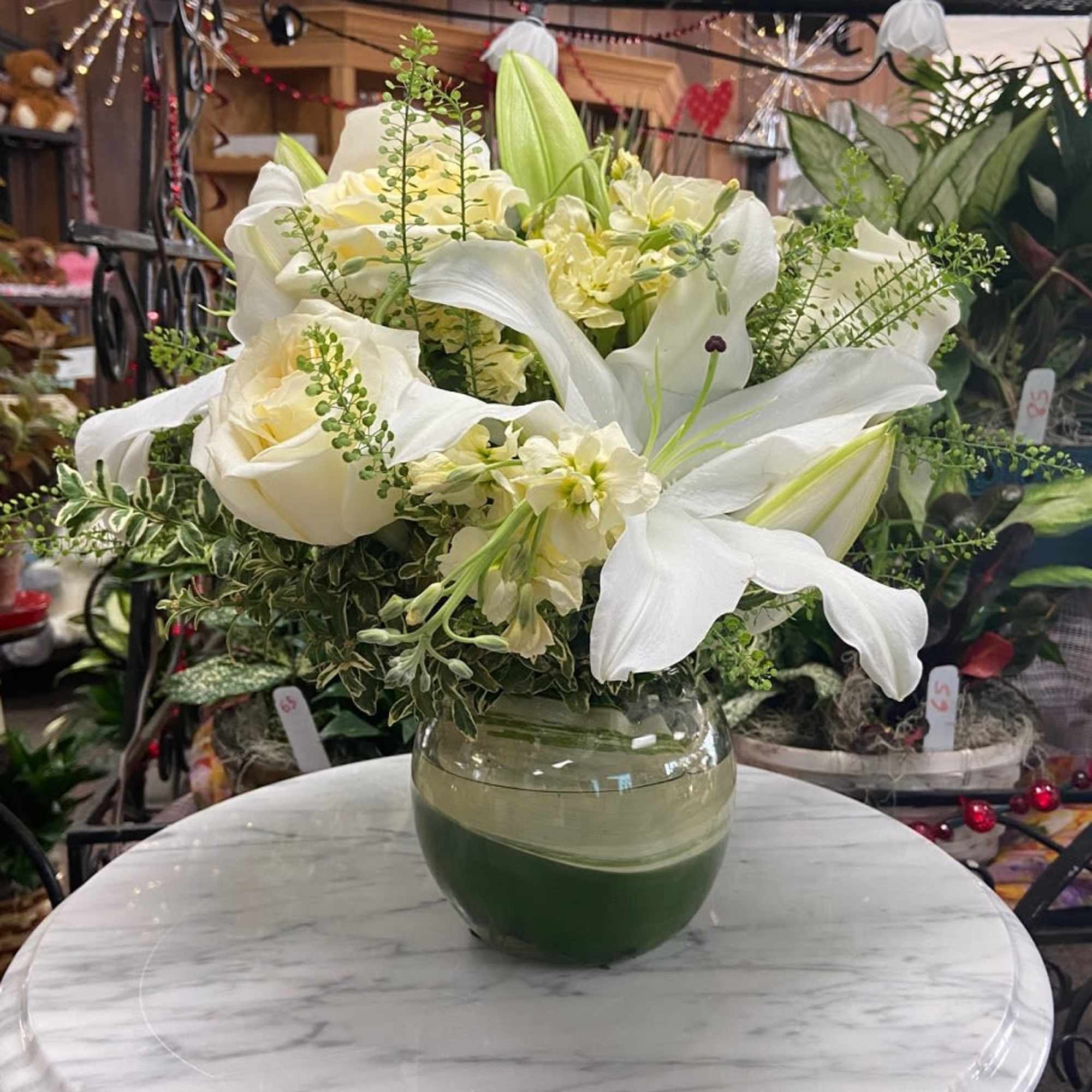 White lilies and cream roses arranged in a round glass vase on a marble table