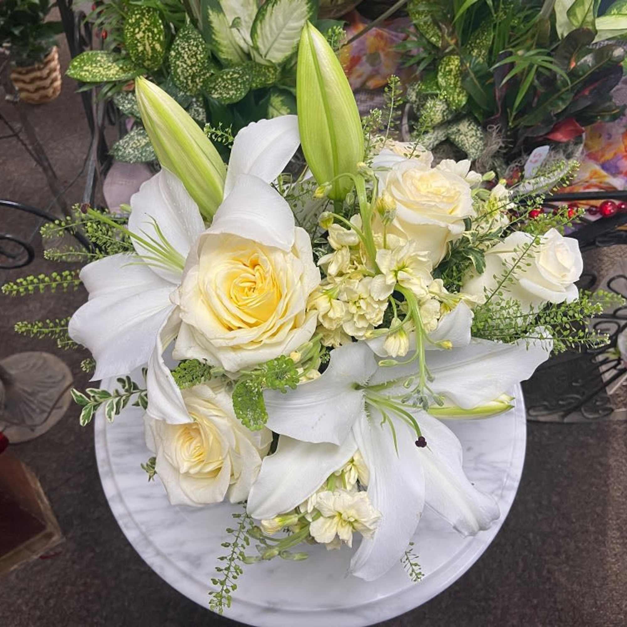 White lilies and cream roses arranged with soft yellow blooms in a compact bouquet