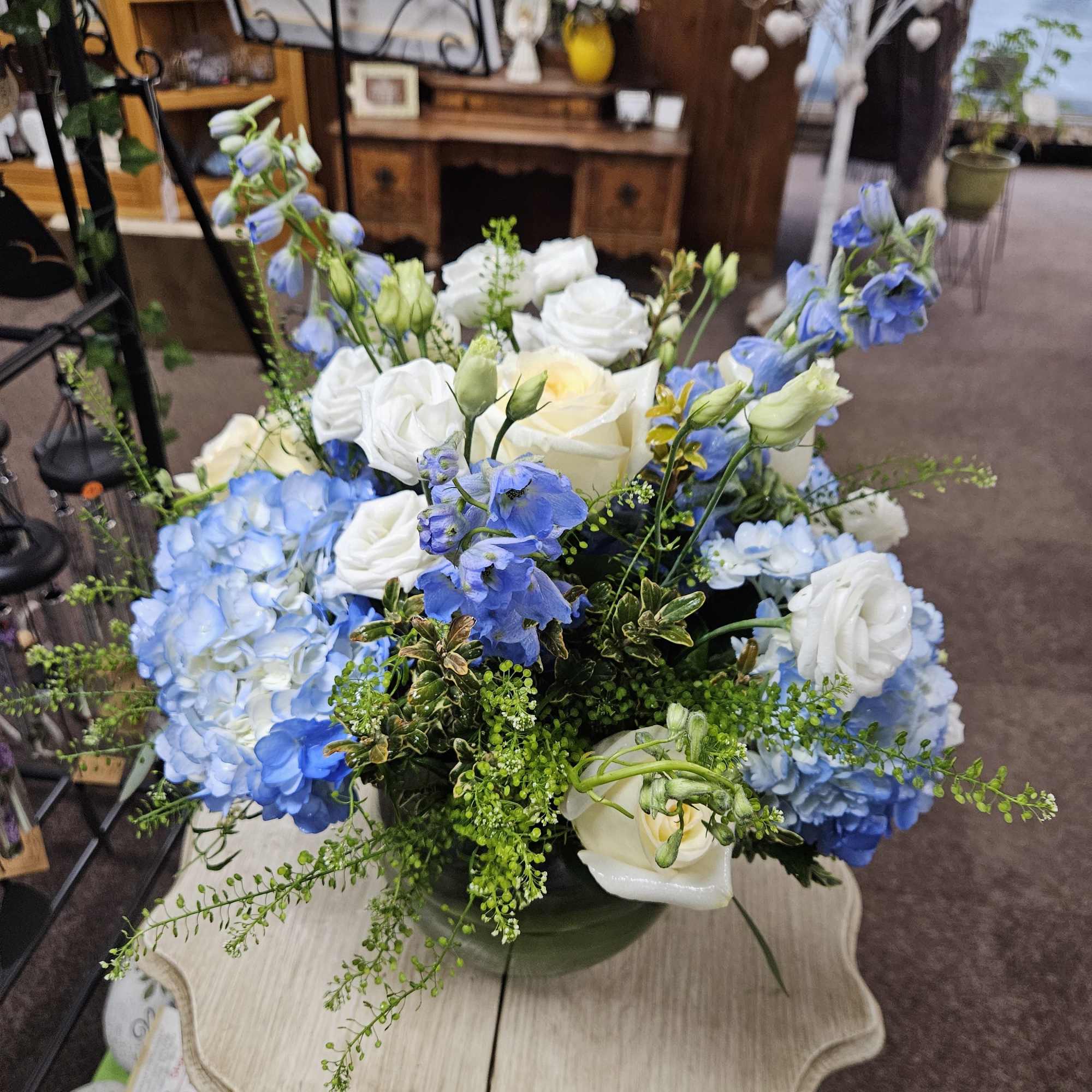 Round arrangement of blue hydrangeas, blue delphinium, and white roses in a green ceramic bowl