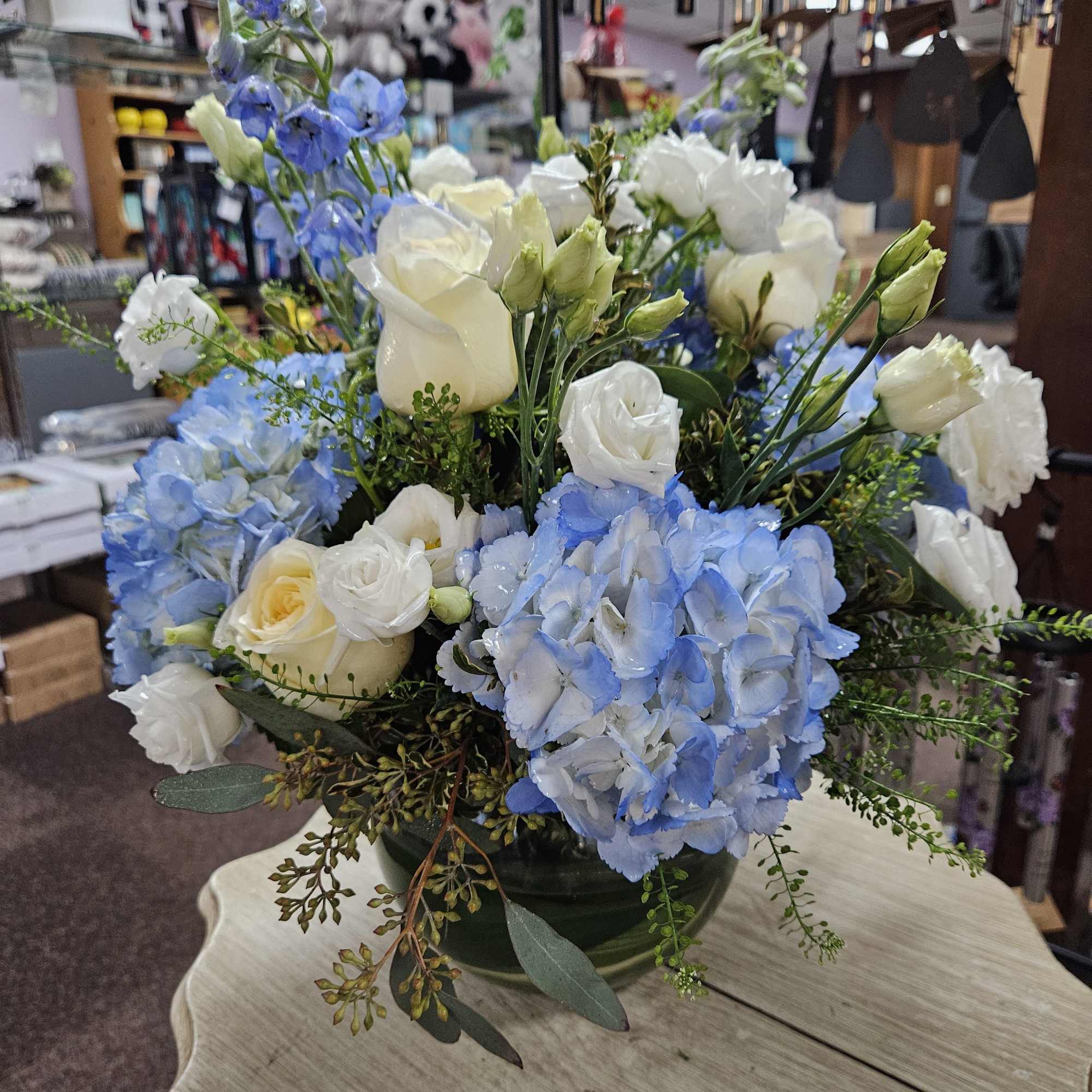 Low arrangement of blue hydrangeas and white roses in a round glass vase.