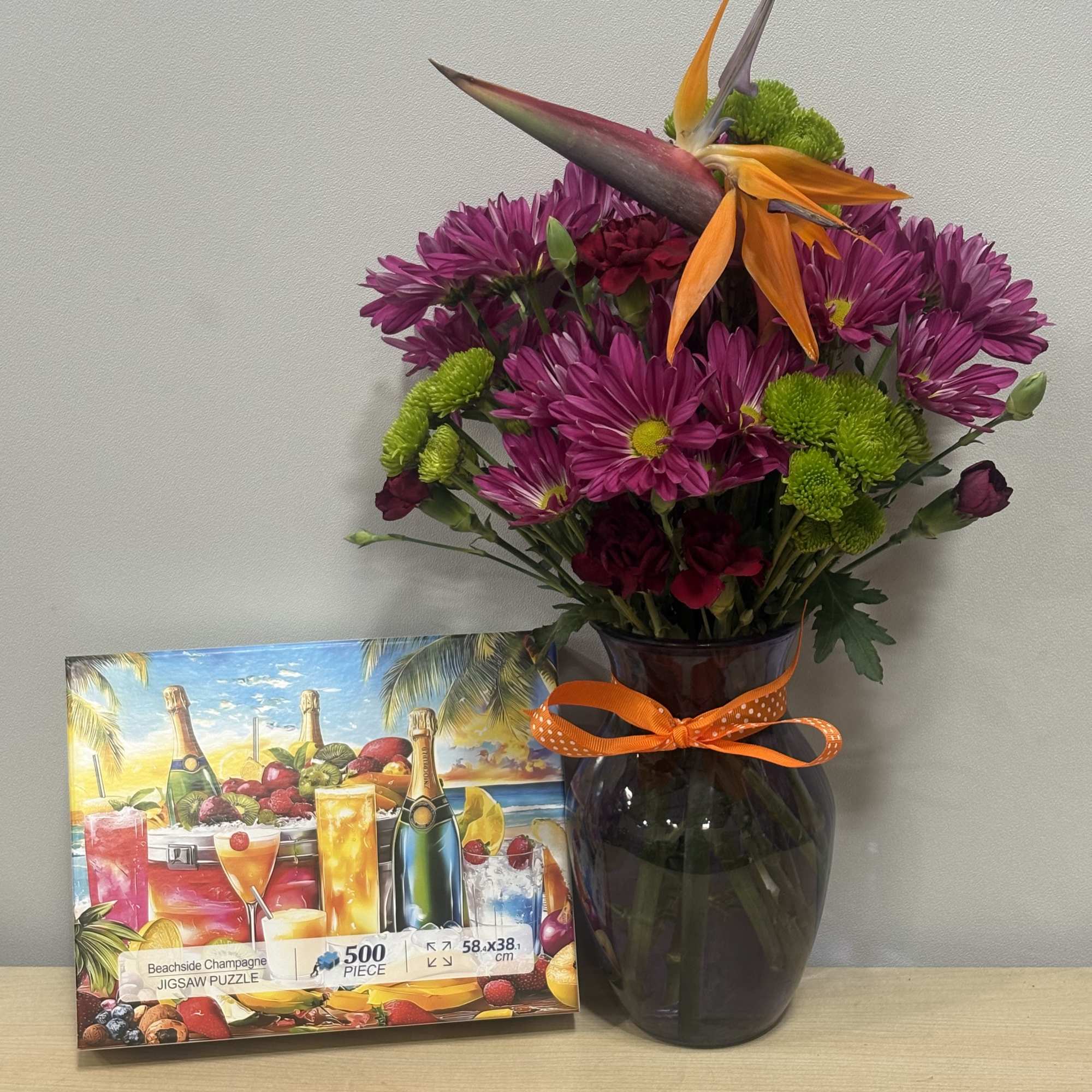 Purple chrysanthemum bouquet in a dark glass vase with an orange ribbon
