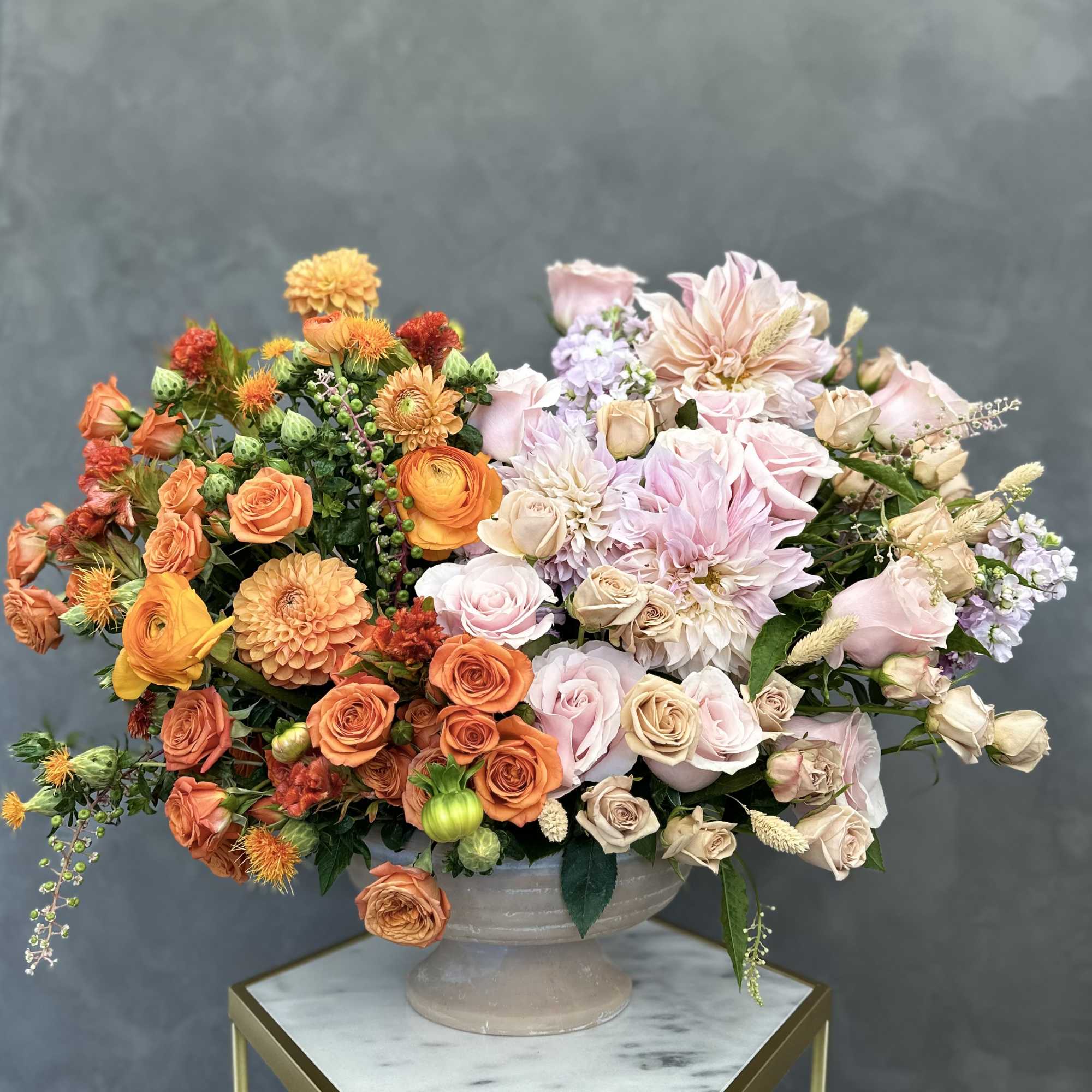 Large mixed bouquet in a gray pedestal vase with orange and blush flowers