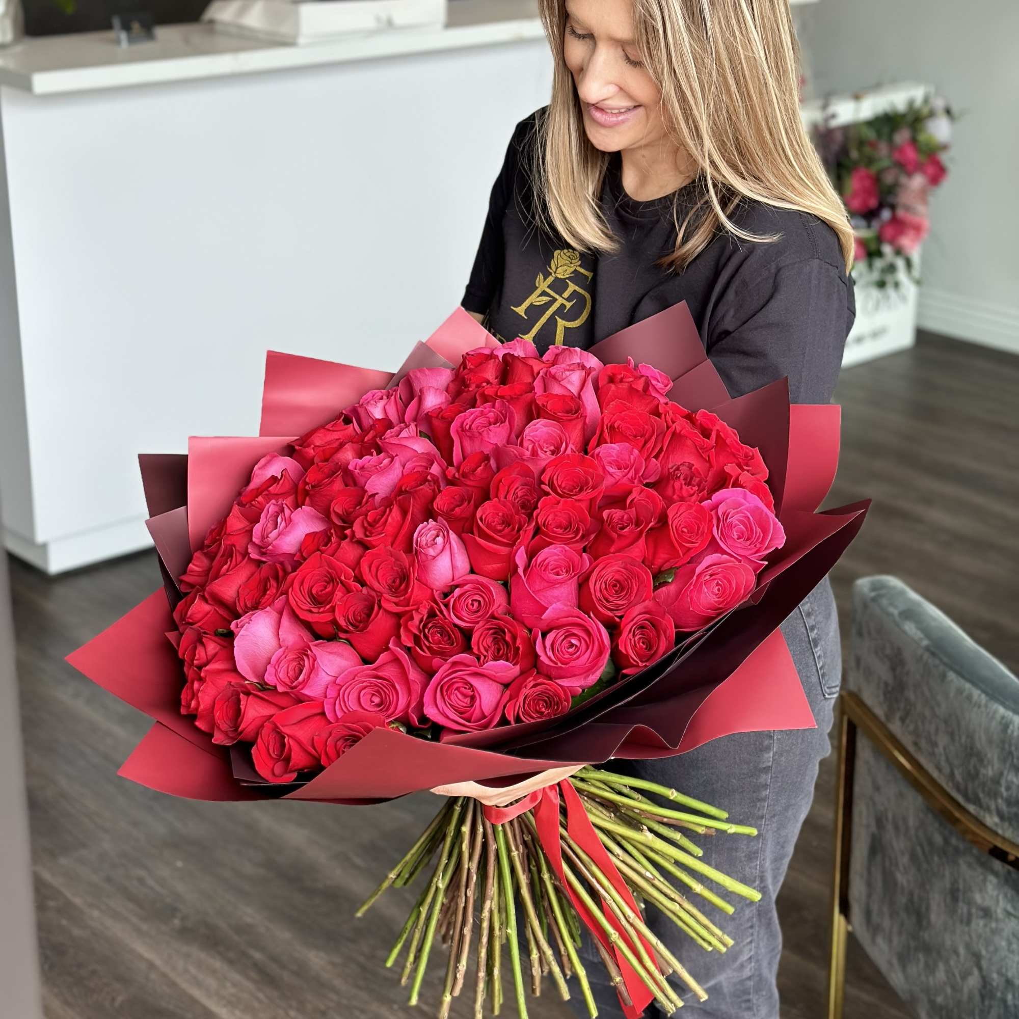 Woman holding a large bouquet of red and pink roses wrapped in burgundy paper