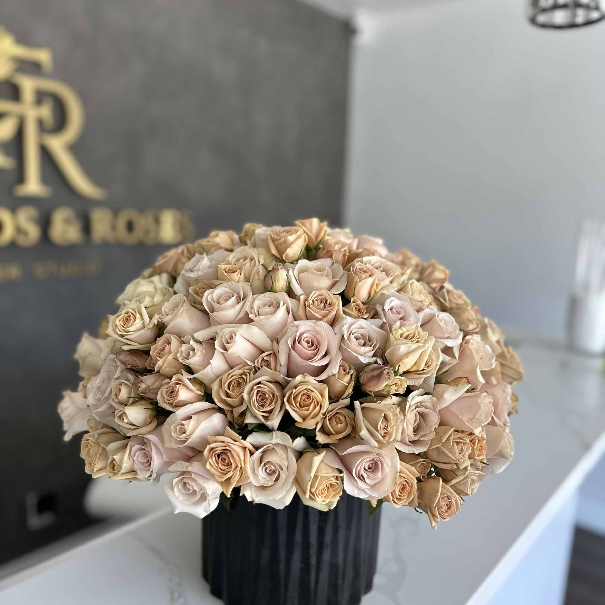 Large bouquet of pale blush and beige roses in a black vase