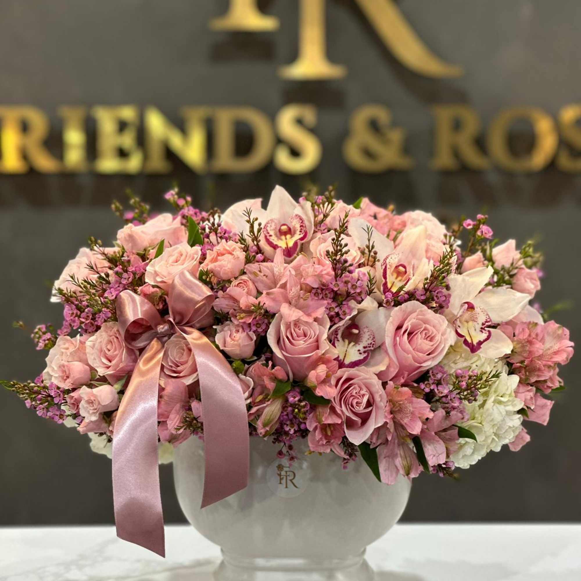 Pink roses and orchids arranged in a white vase with a satin ribbon