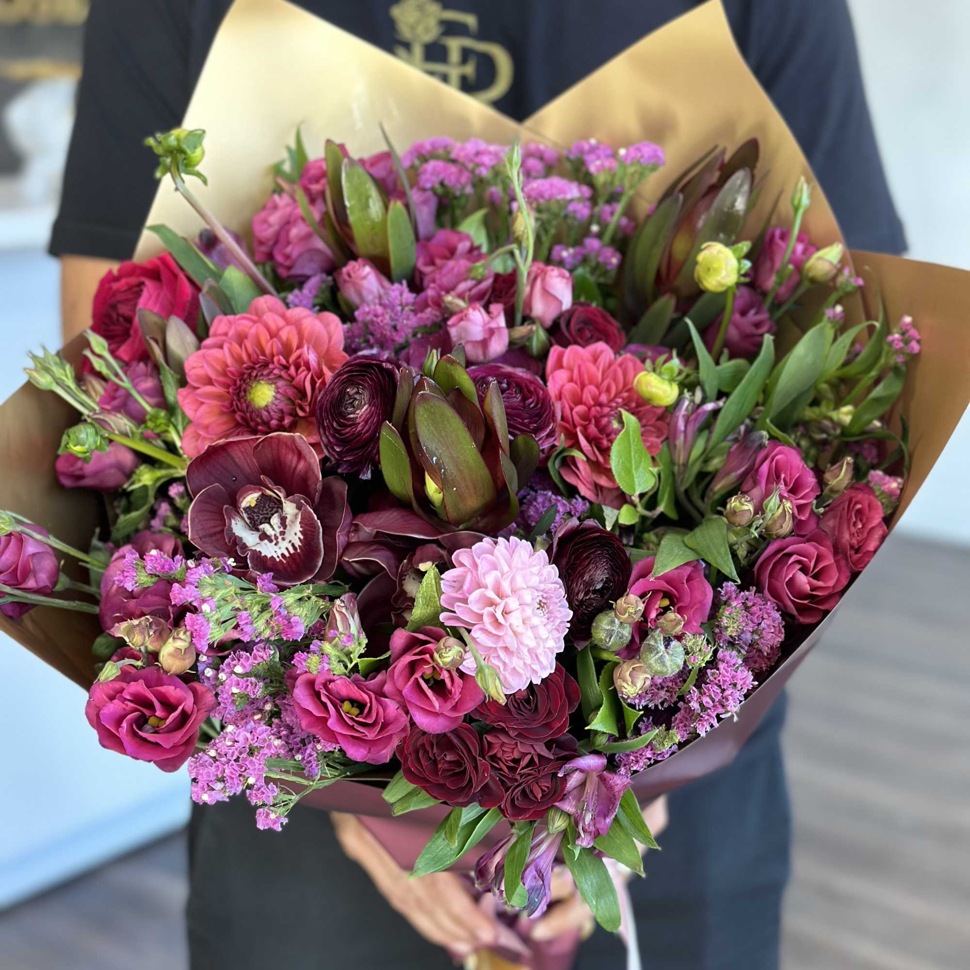 Handheld bouquet of pink and burgundy flowers wrapped in brown paper