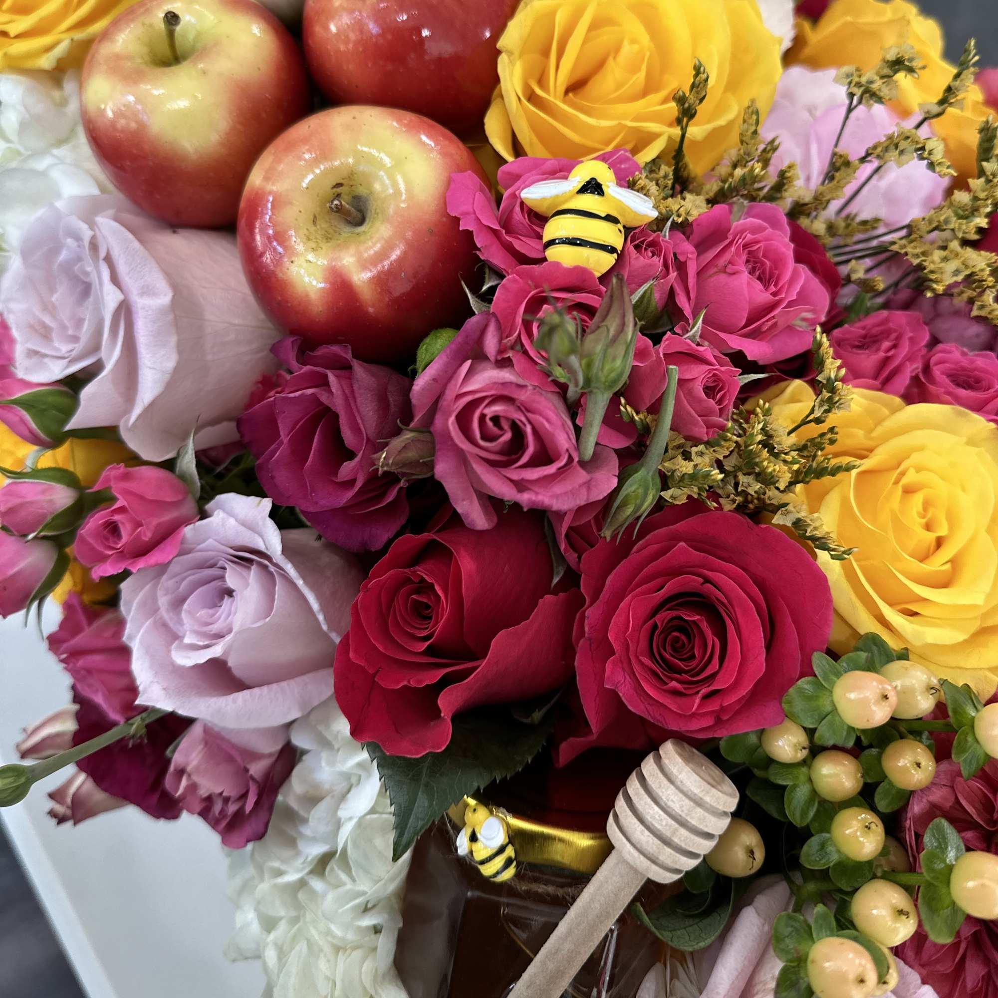Bouquet of roses with apples, honeybee decorations, and a honey dipper