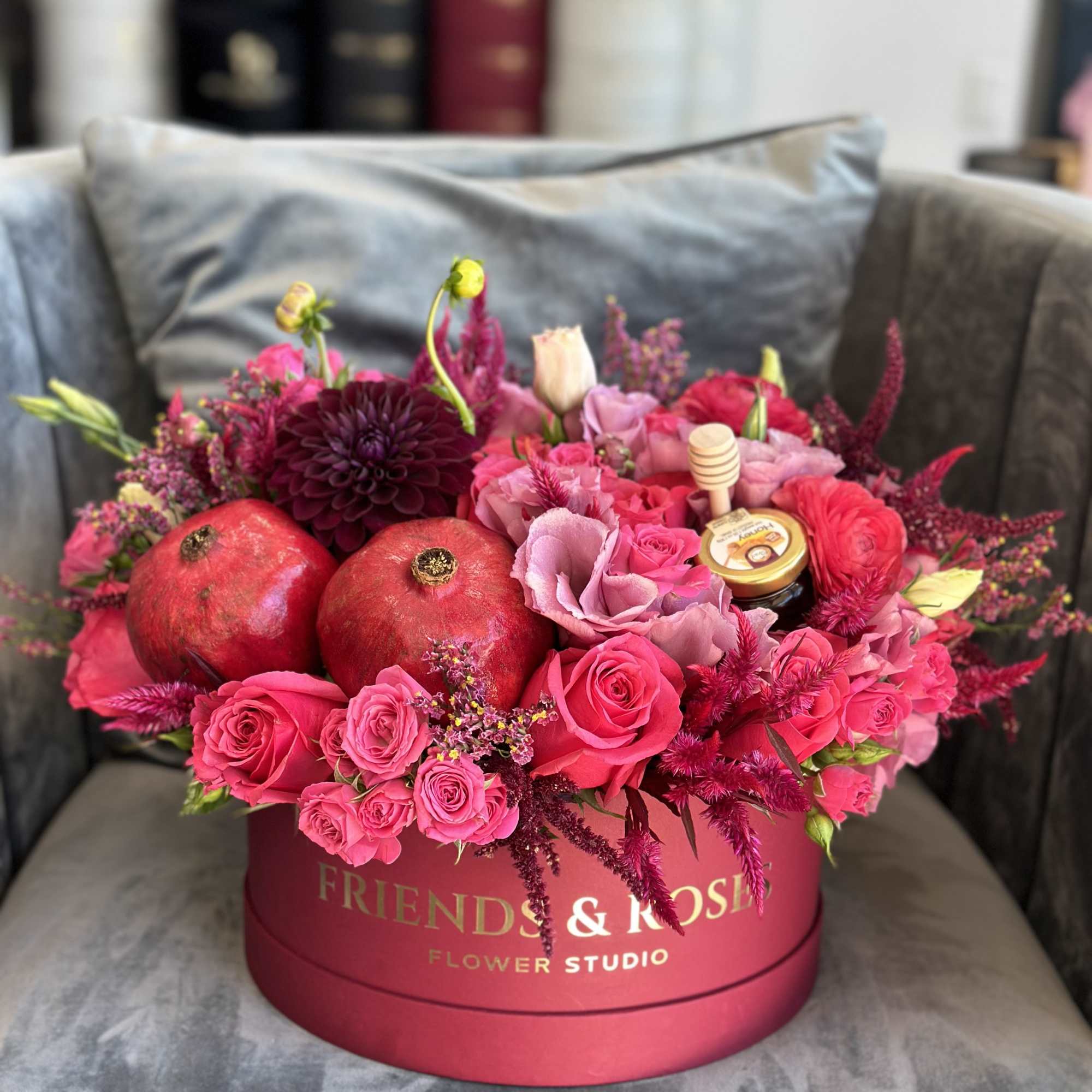 Pink and red flower arrangement in a round box with pomegranates and a honey jar