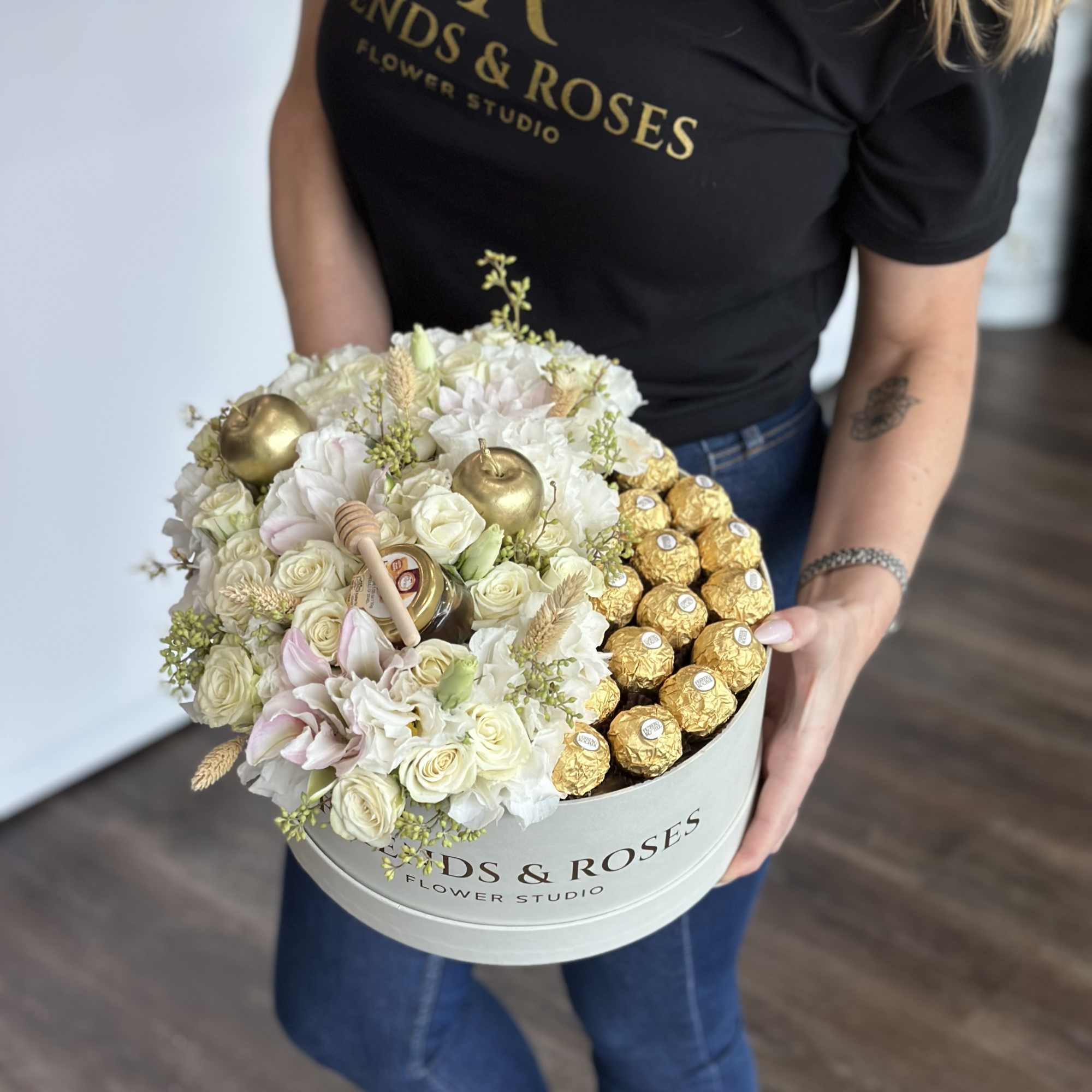 Round box of white roses and gold-wrapped chocolates held by a woman