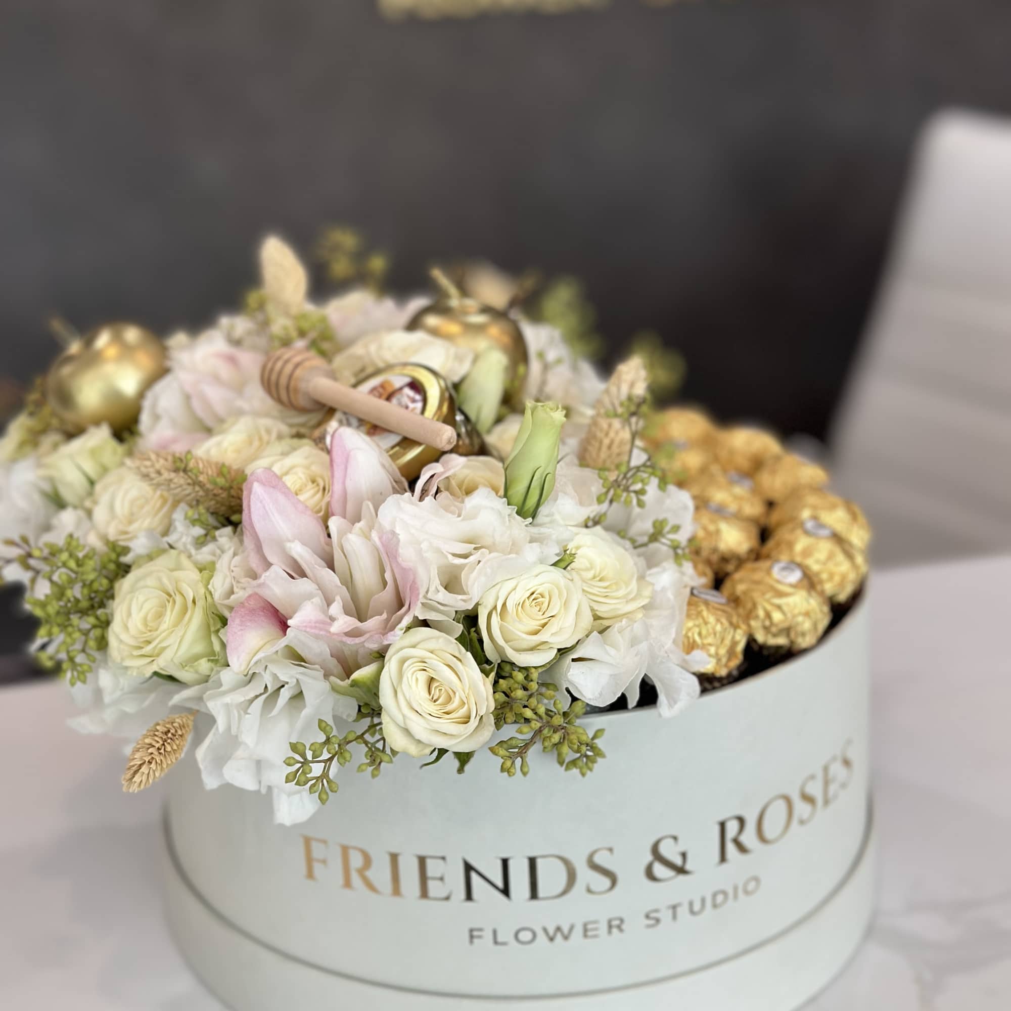 Round box of white and blush roses with gold chocolates on top
