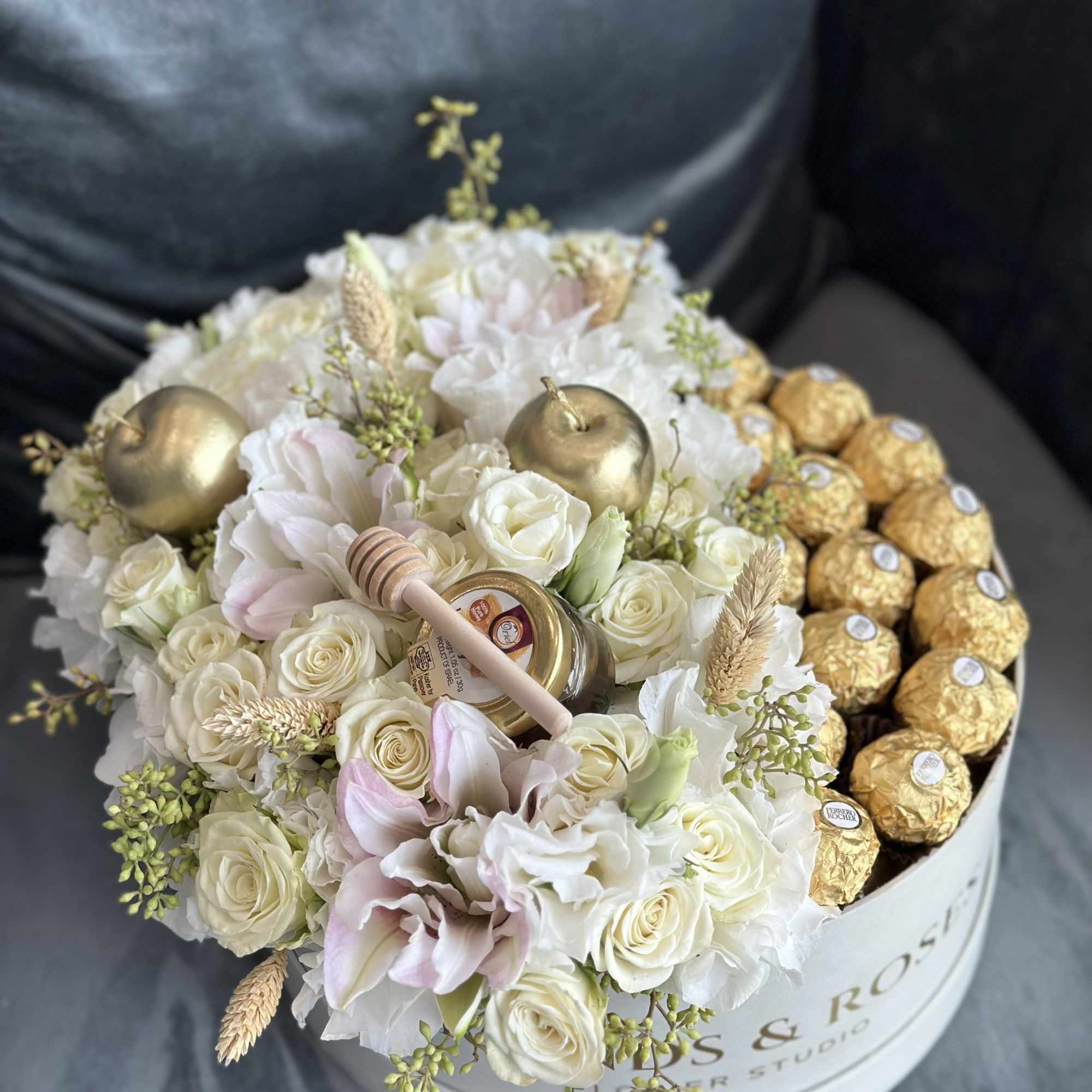 White and blush roses arranged with gold Ferrero Rocher chocolates in a round box