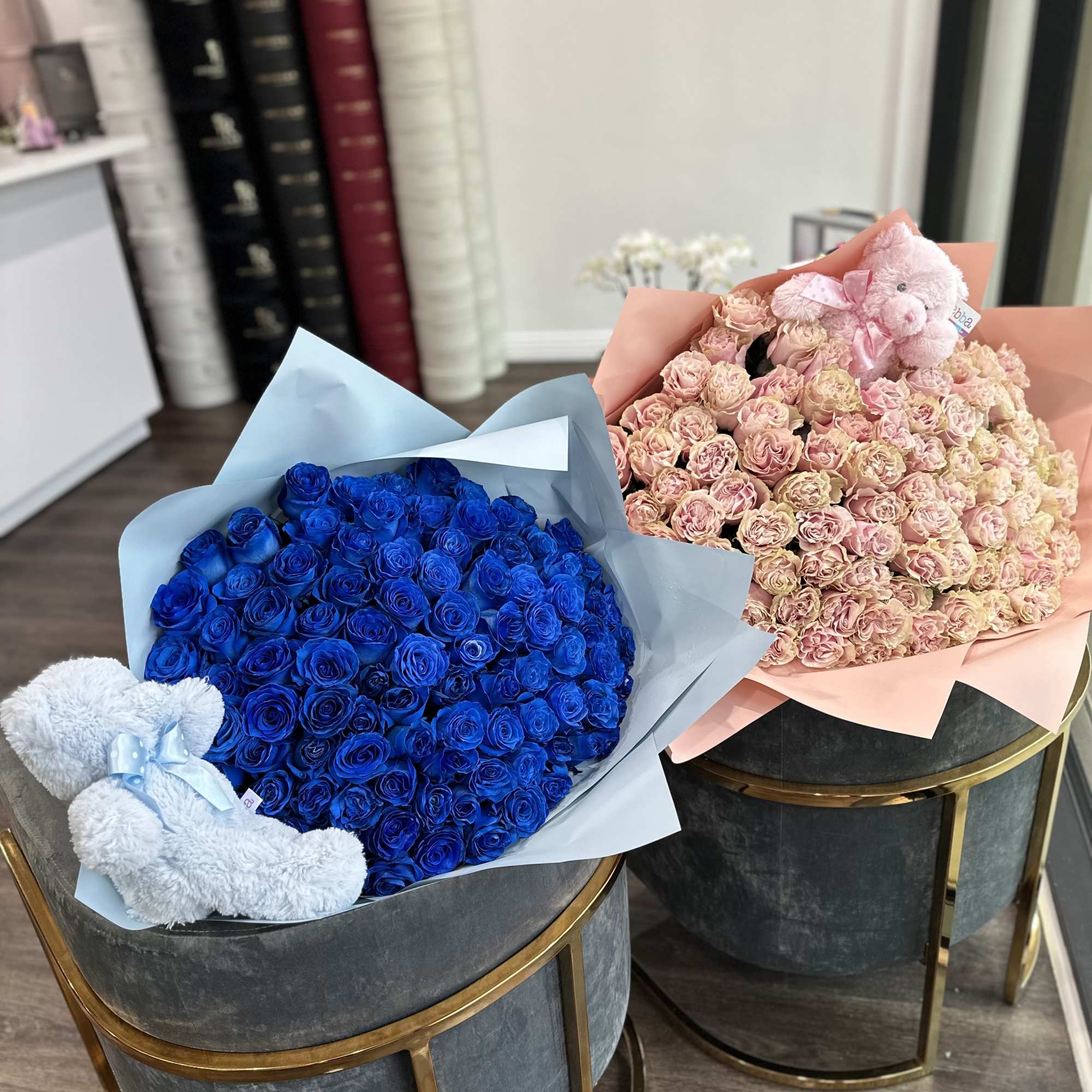 Two large rose bouquets in blue and blush wrapping, one with a teddy bear