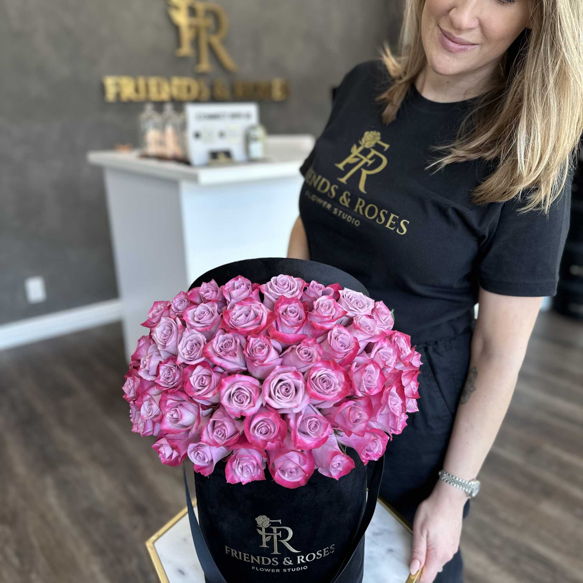Pink roses arranged in a black hatbox held by a woman