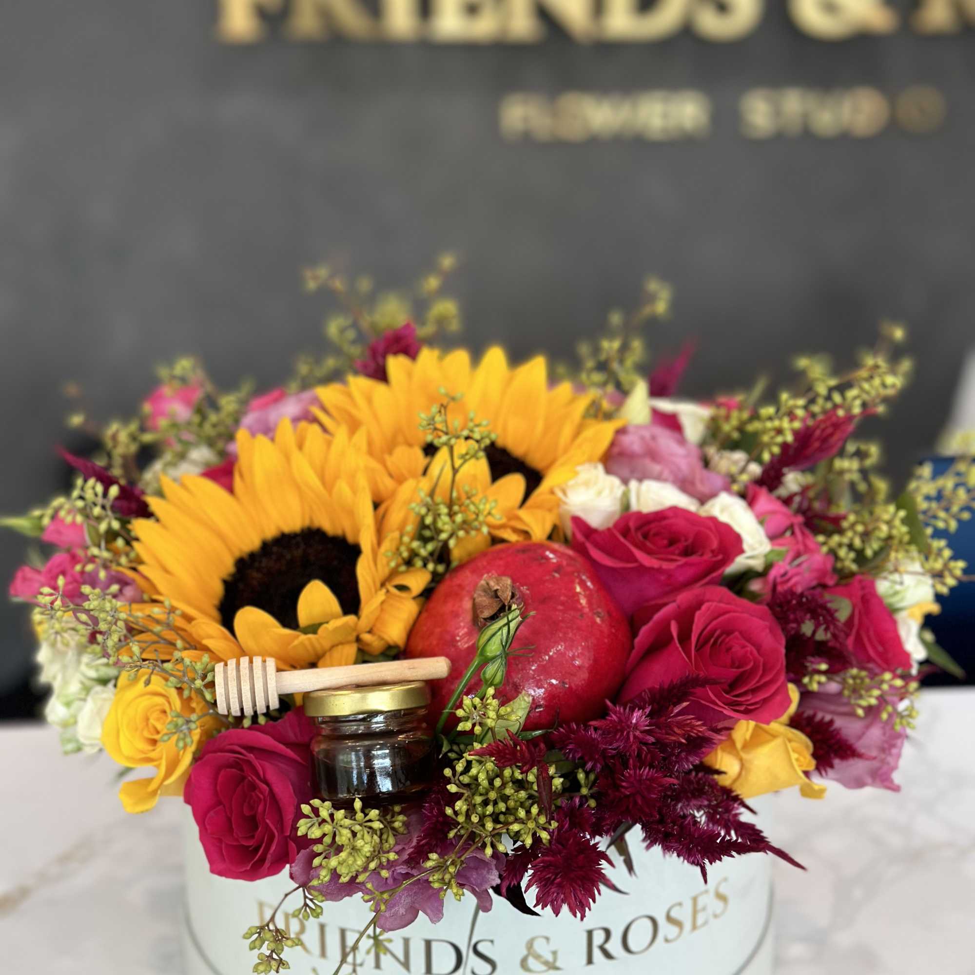 Bouquet with sunflowers, red roses, and a pomegranate in a round box