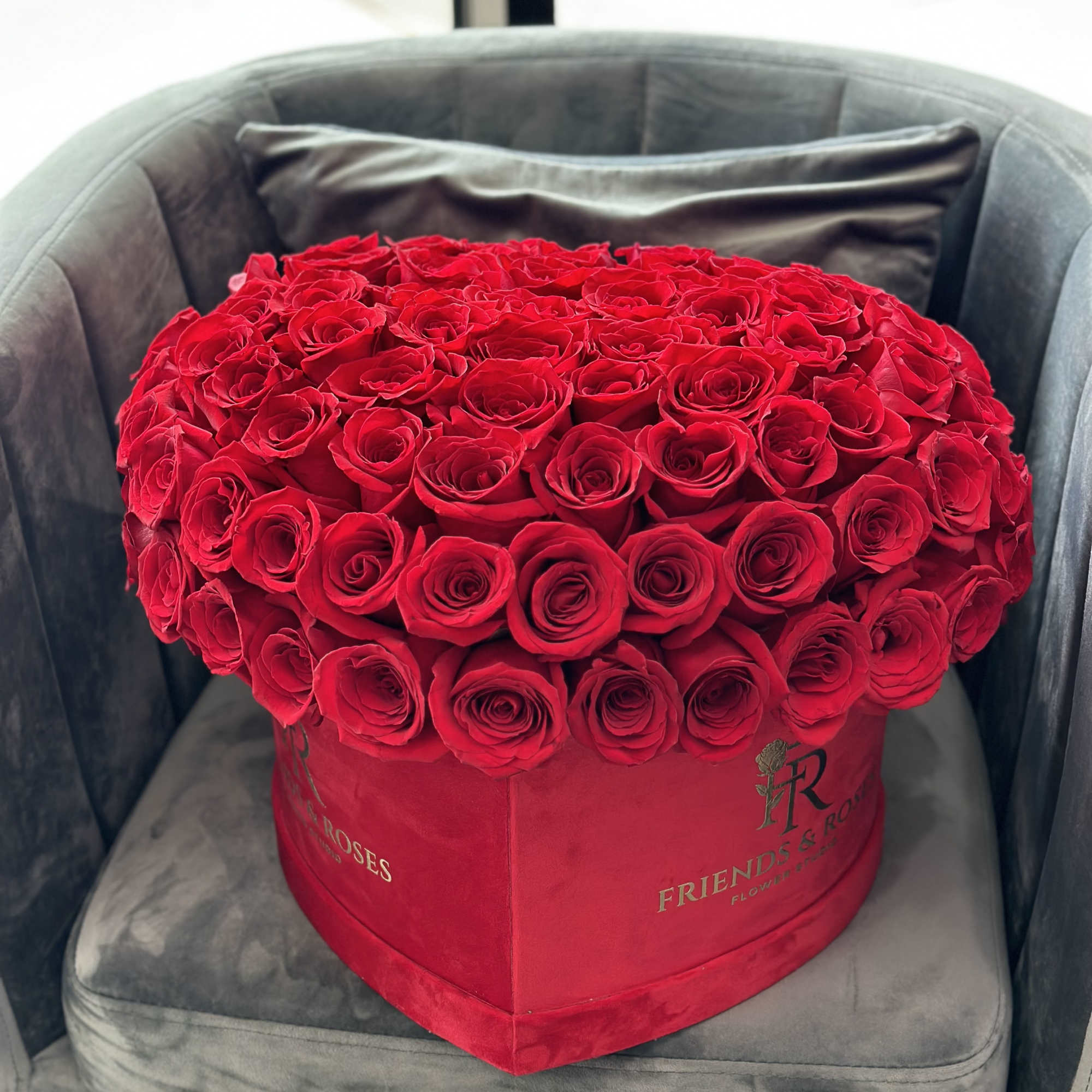 Large red rose arrangement in a red heart-shaped box on a gray chair