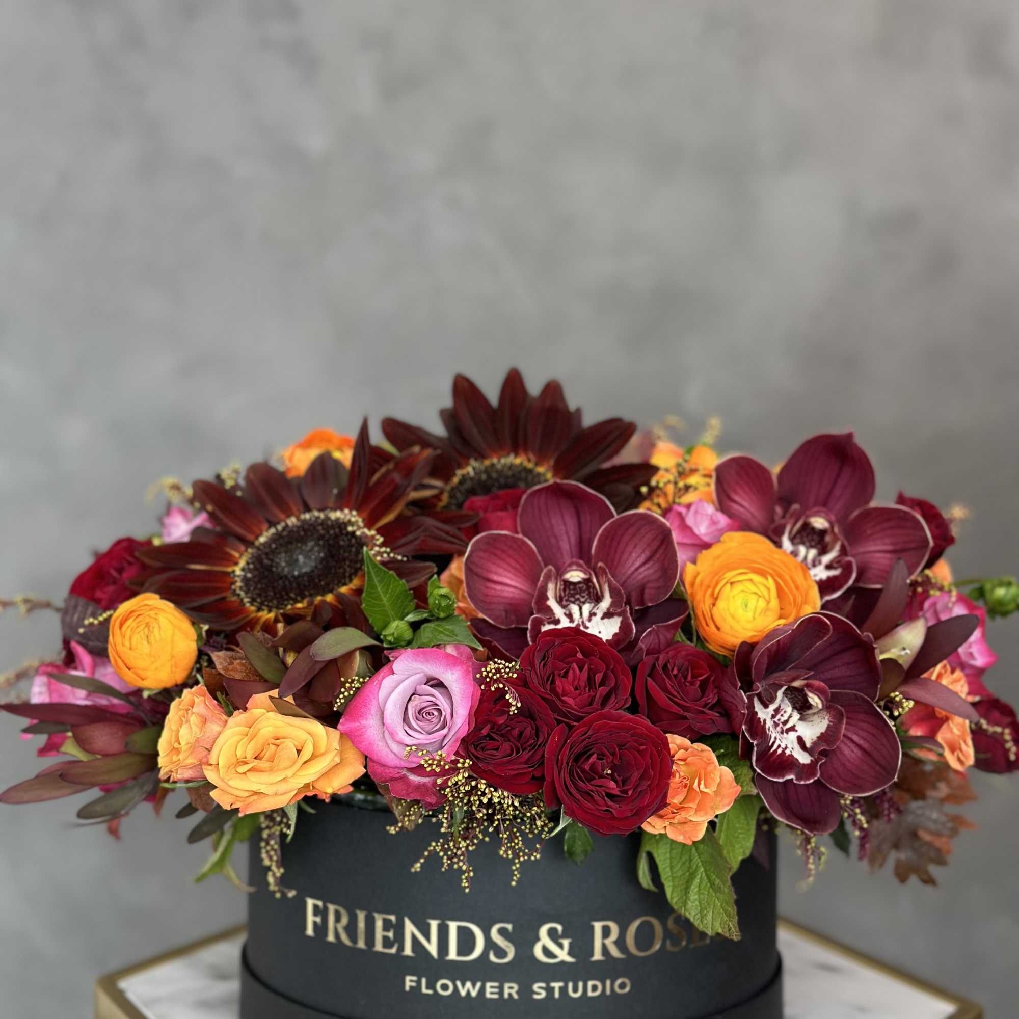 Round box arrangement with burgundy orchids, roses, and sunflowers