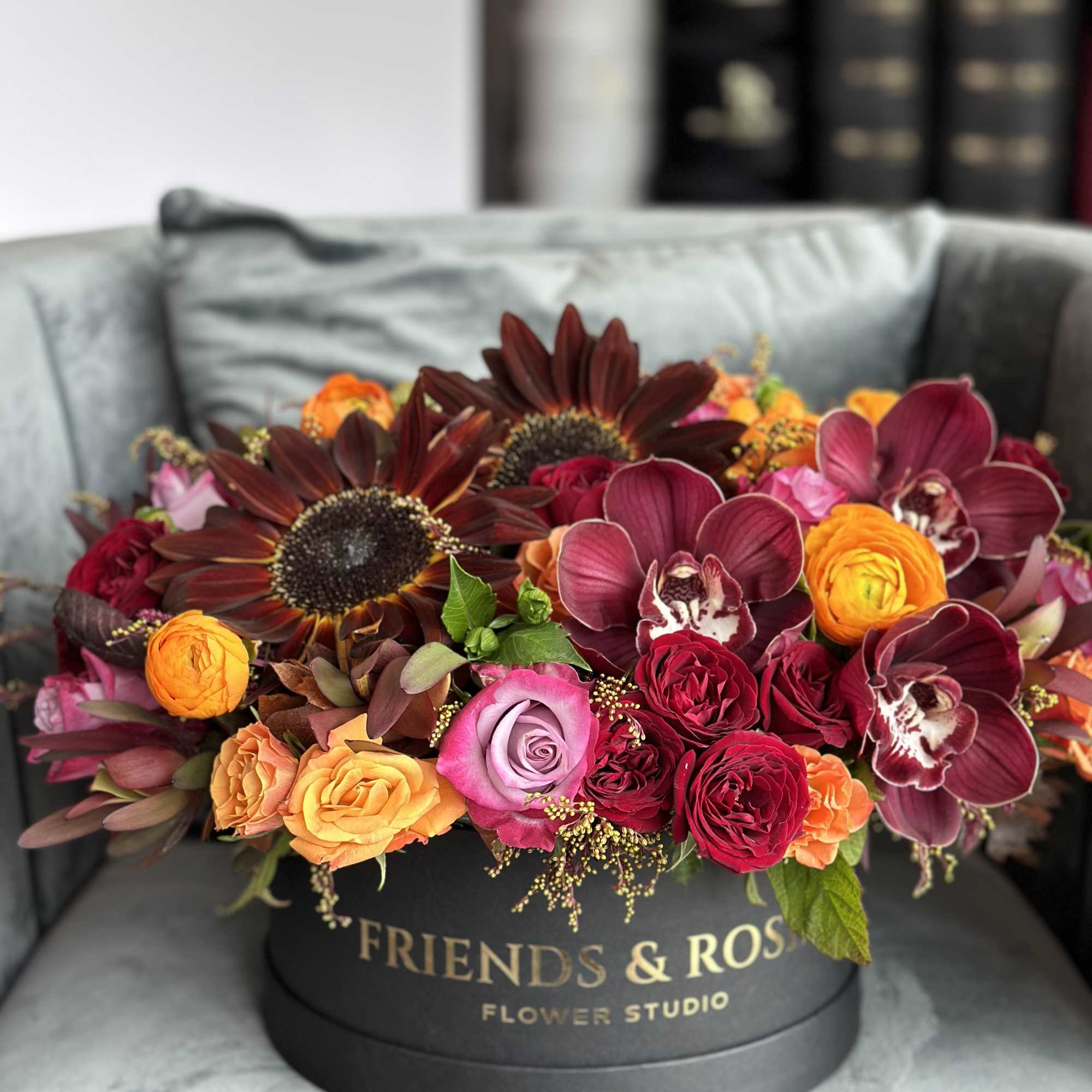 Mixed bouquet of roses, orchids, and sunflowers in a black round box