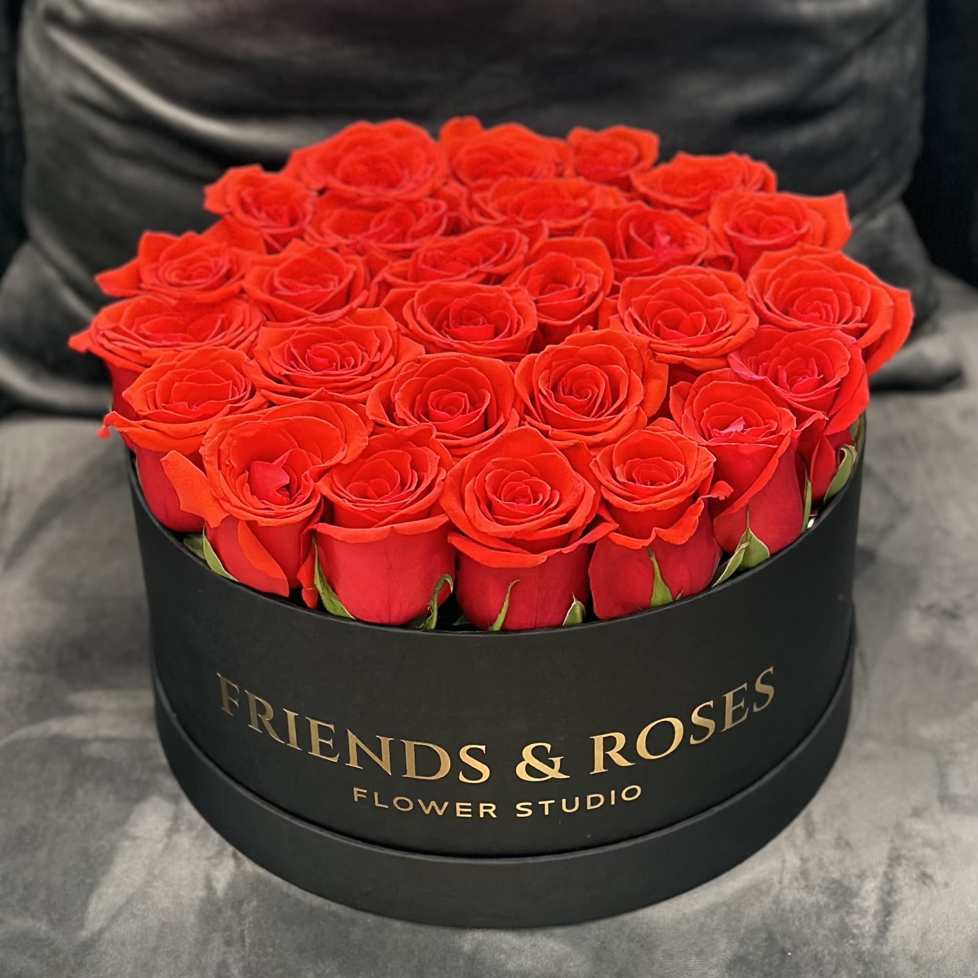 Round box of red roses with gold lettering on the front