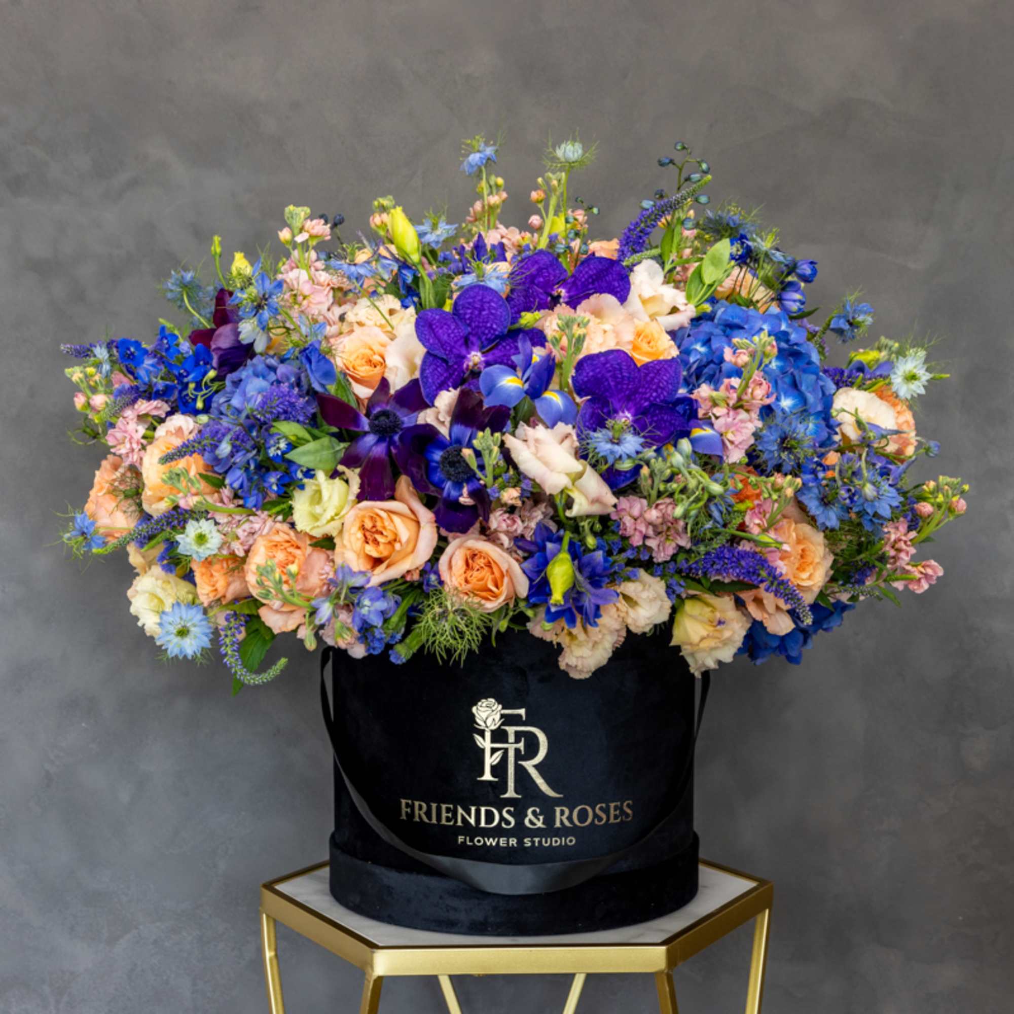 Large mixed bouquet in a black hatbox with blue, purple, peach, and pink flowers