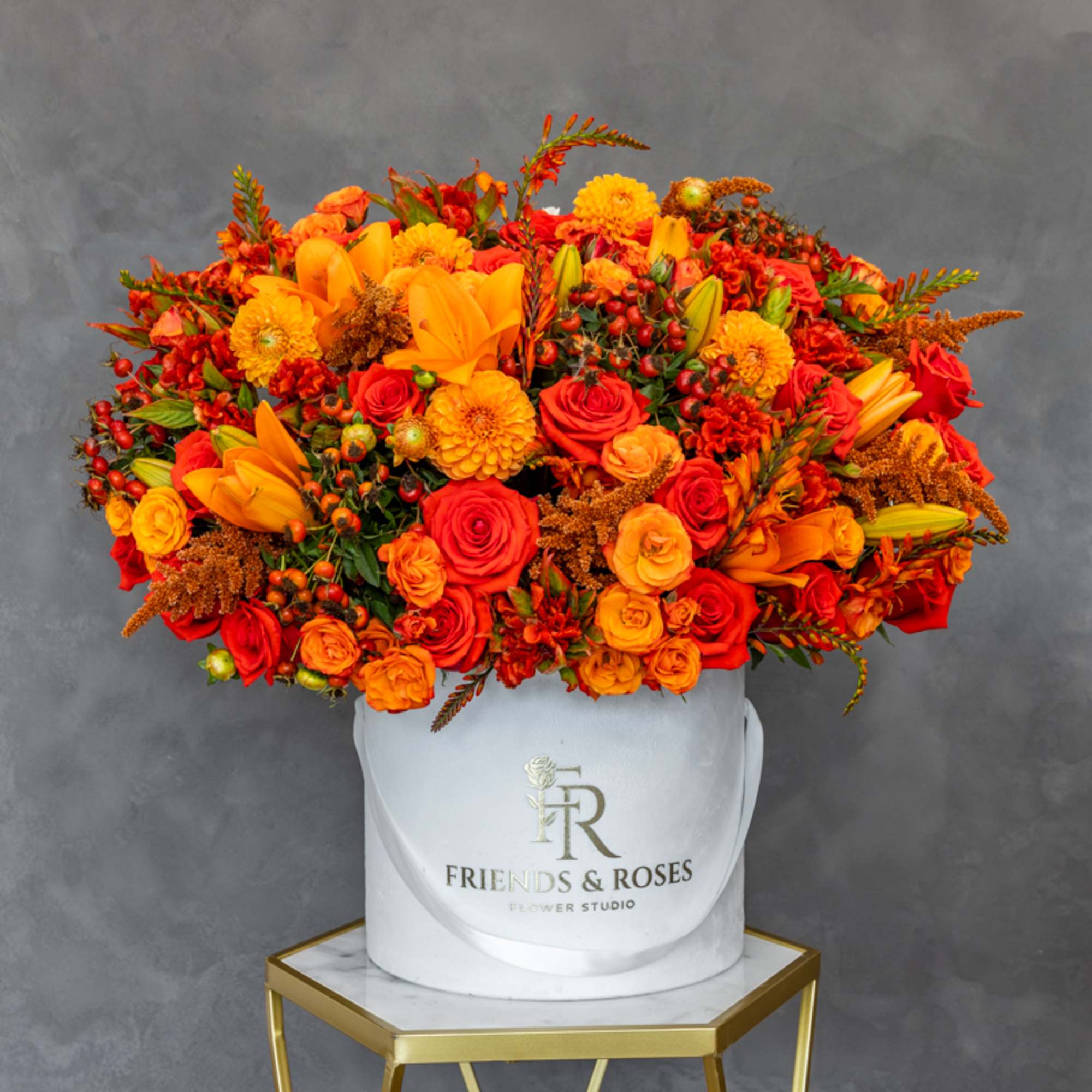 Large orange and red flower arrangement in a white hatbox