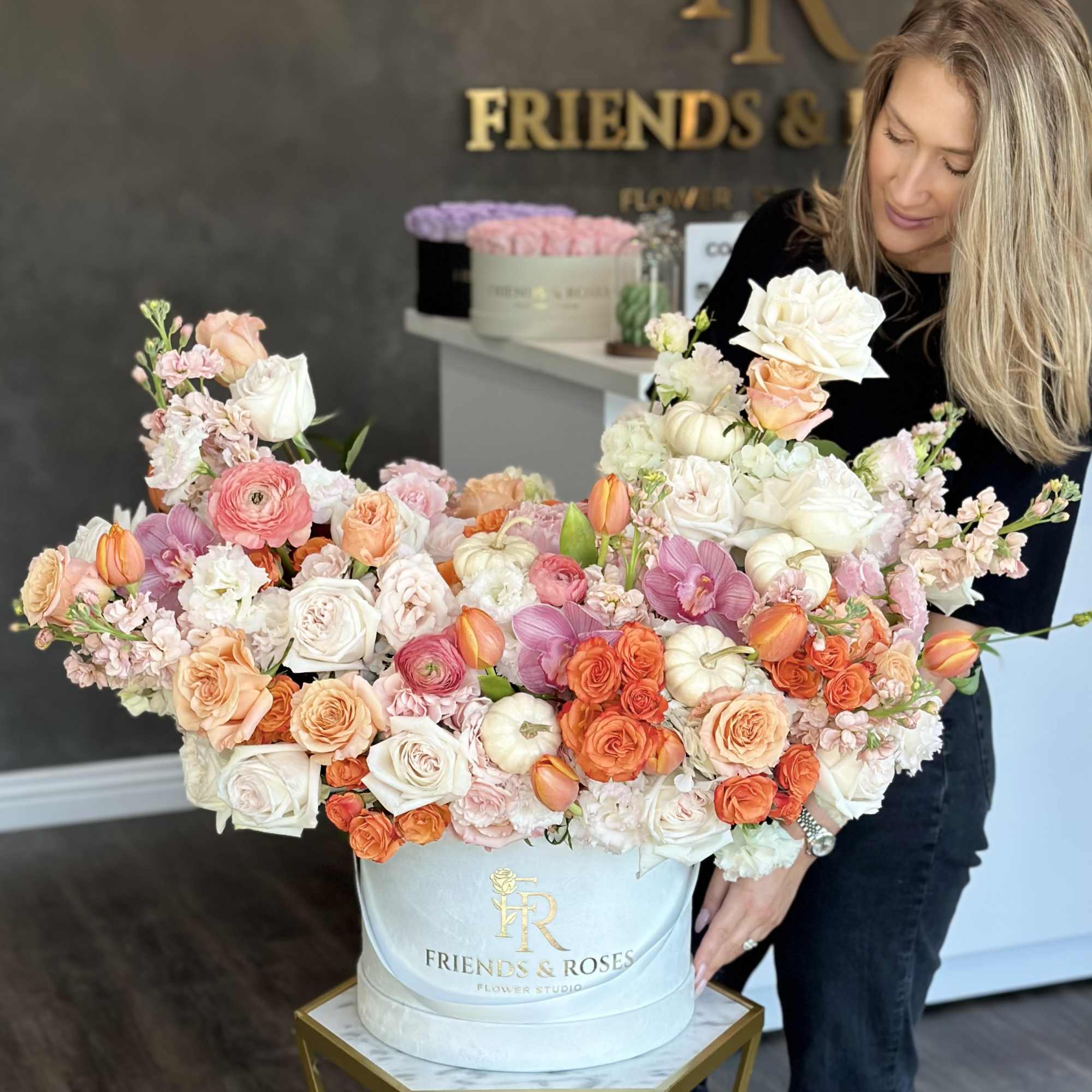 Large pastel flower arrangement in a white hatbox held by a woman