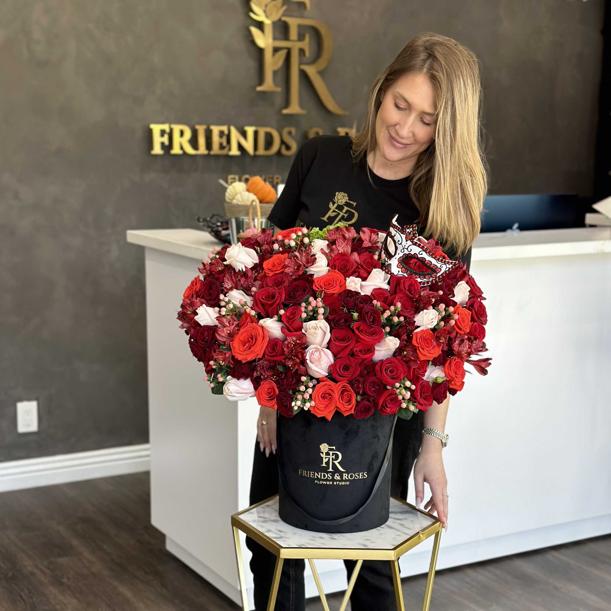 Woman holding a large red and white rose arrangement in a black hatbox
