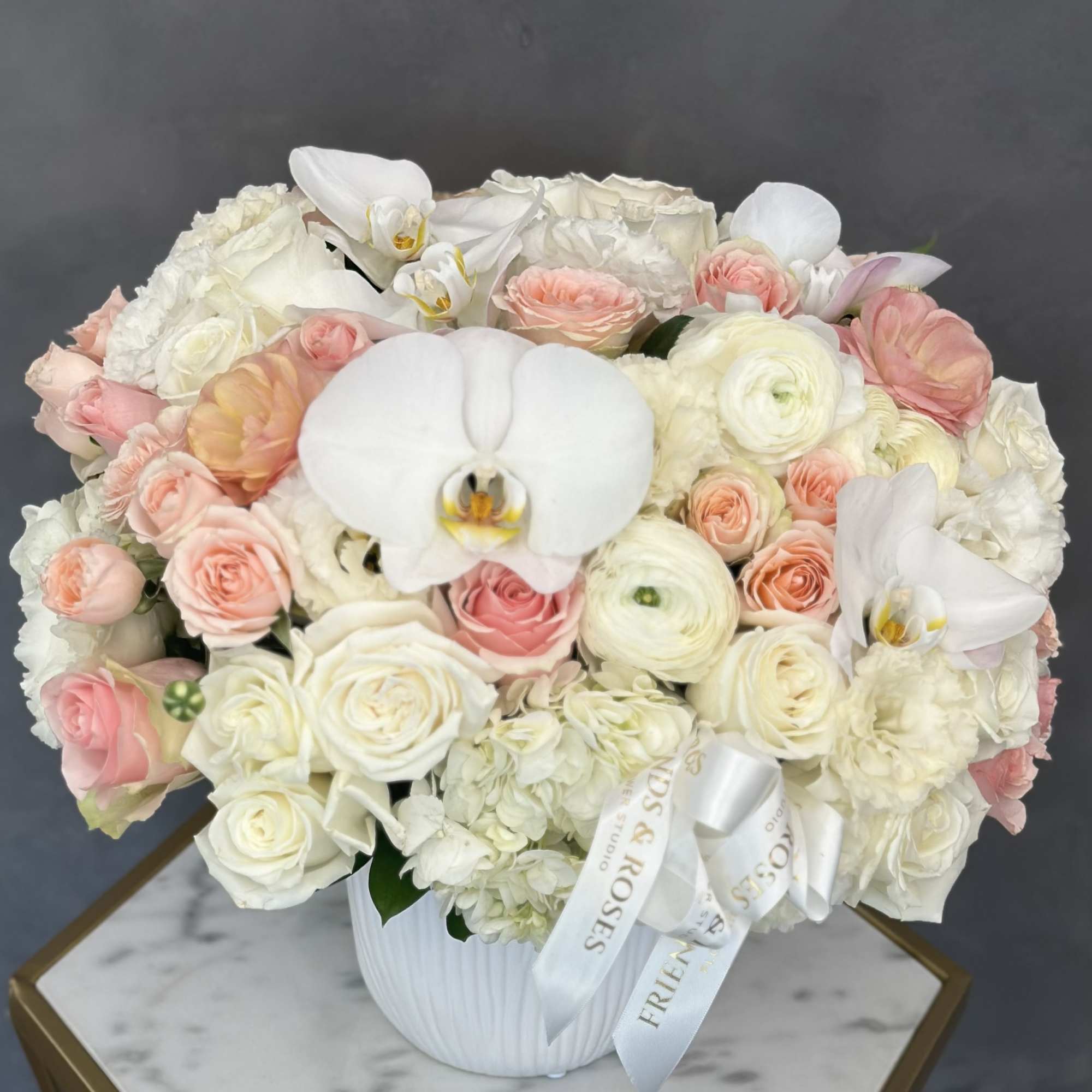 White and blush floral arrangement in a white vase with ribbon.