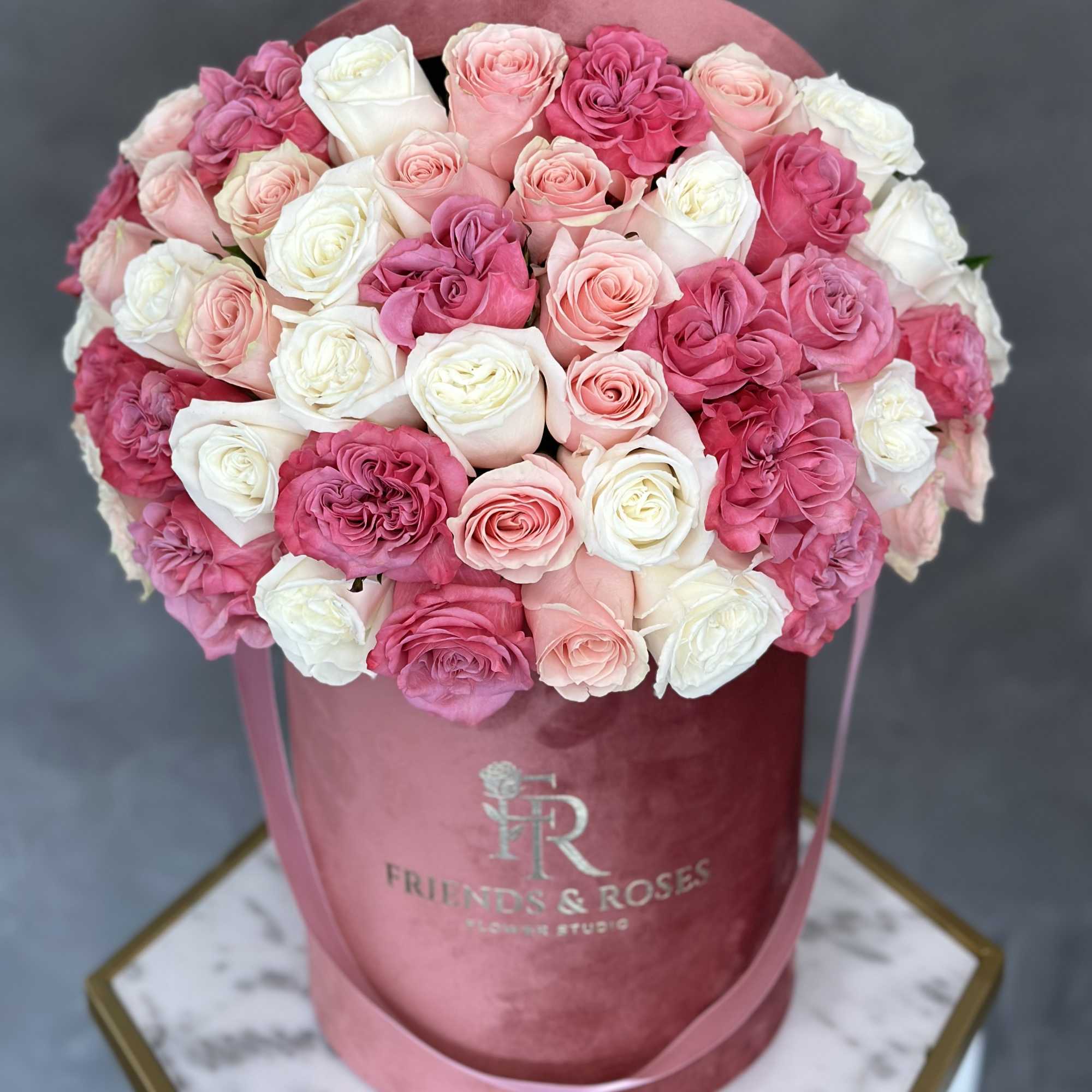 Pink and white roses arranged in a round velvet hatbox