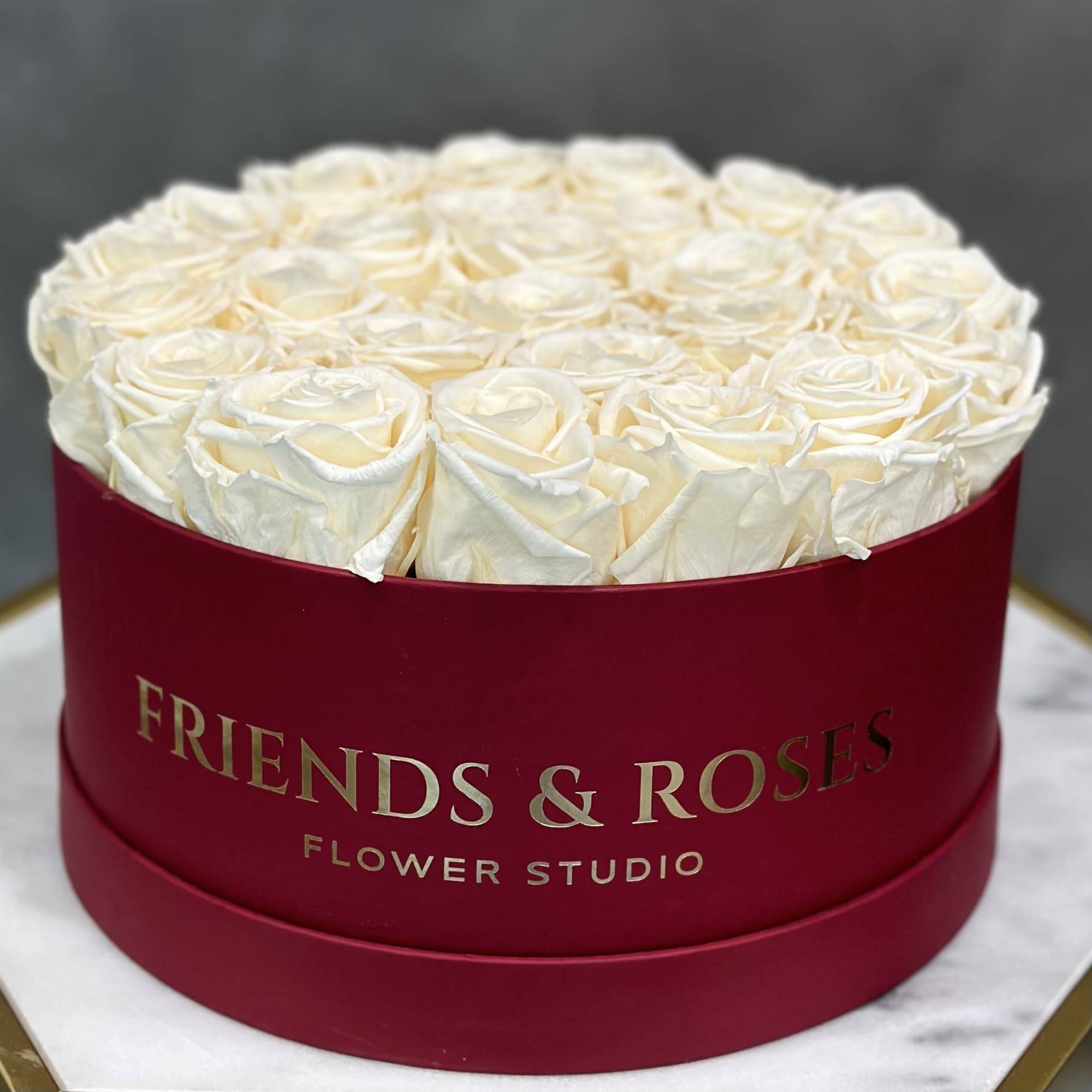 Round box of white roses with a red ribboned container