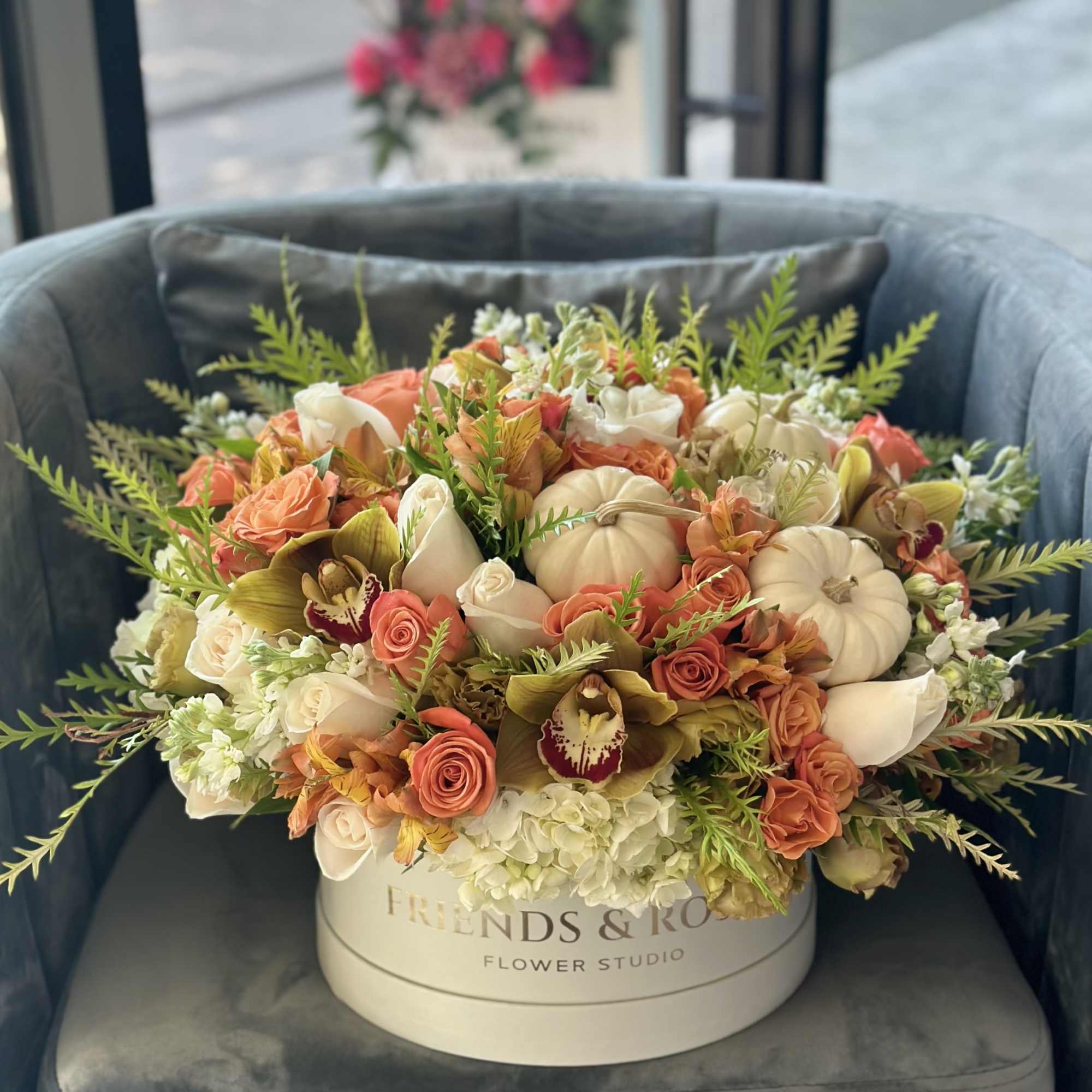 Peach and white floral arrangement in a round hatbox with pumpkins