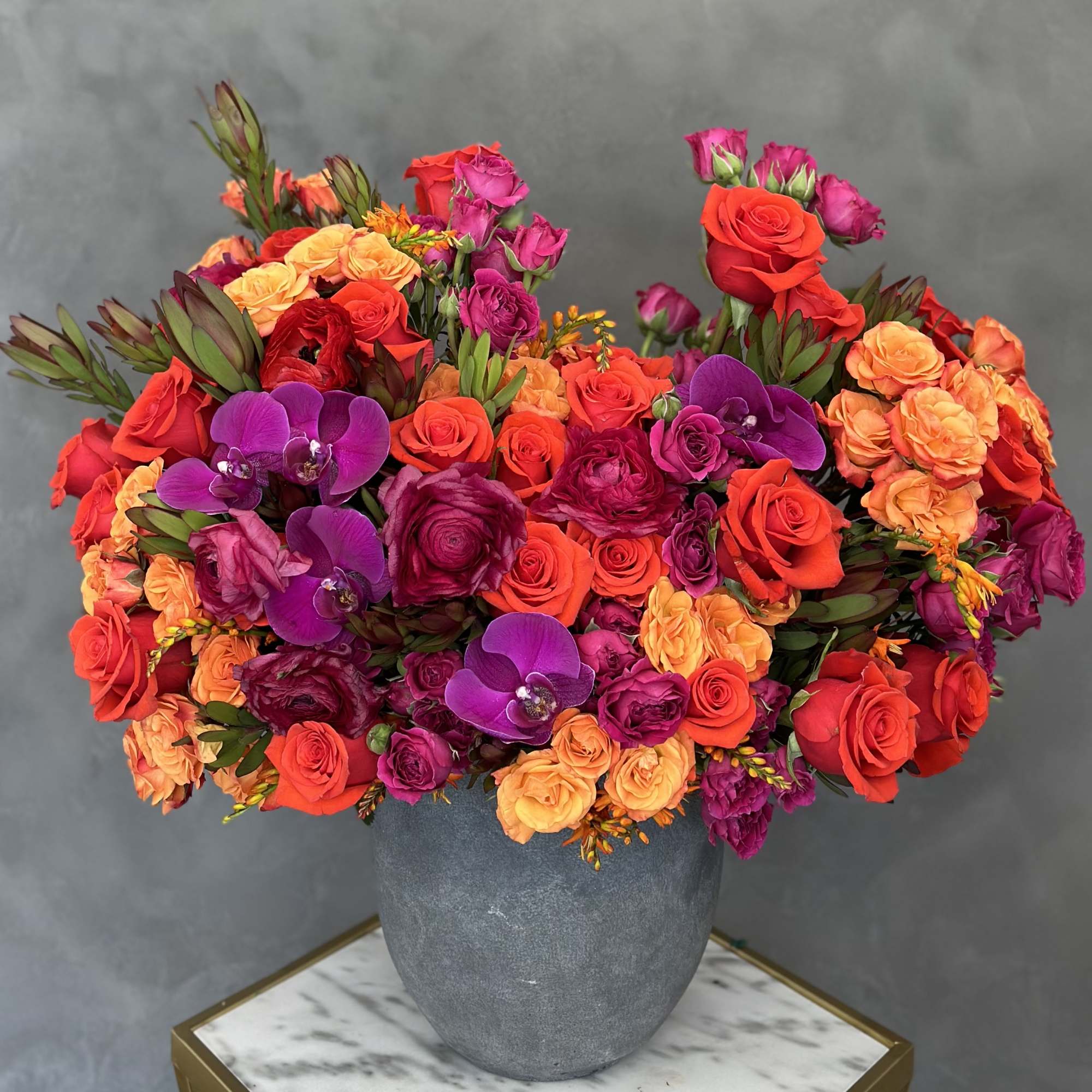 Bright mixed bouquet of roses and orchids in a gray vase