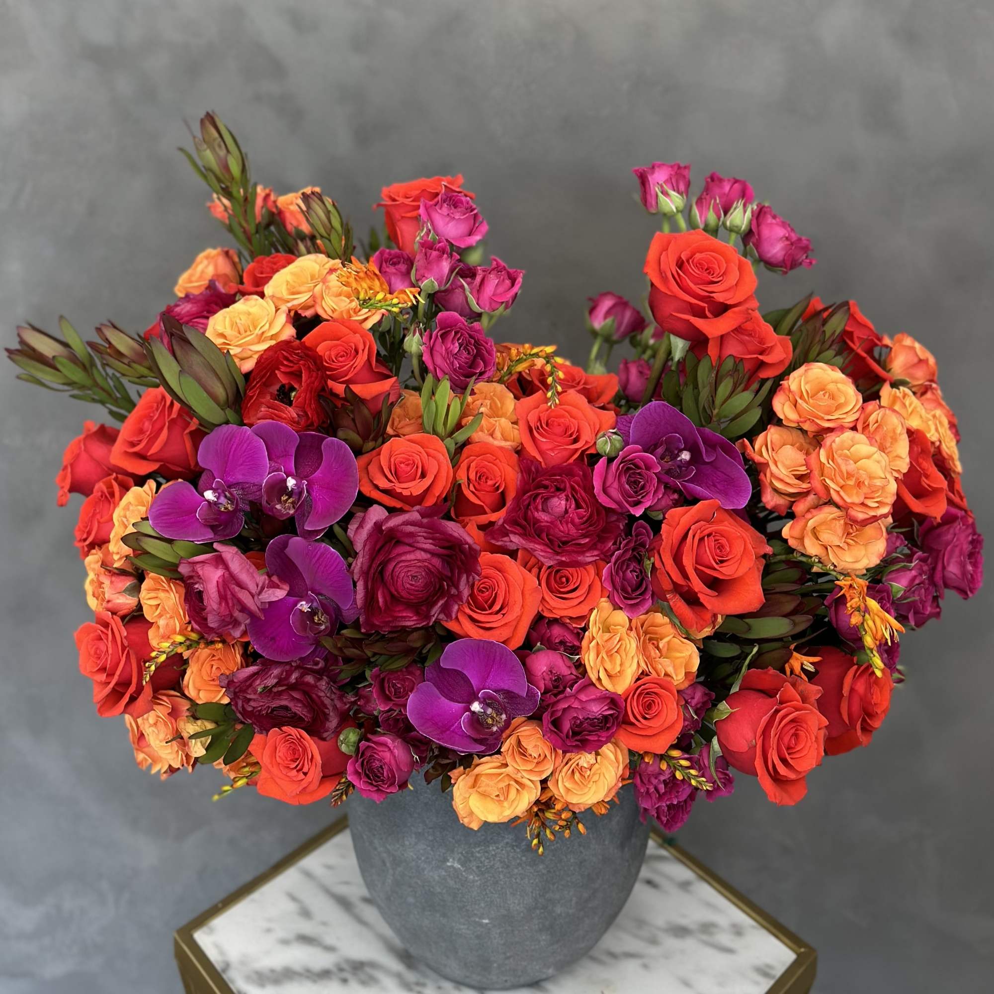 Bright mixed roses and purple orchids in a gray vase