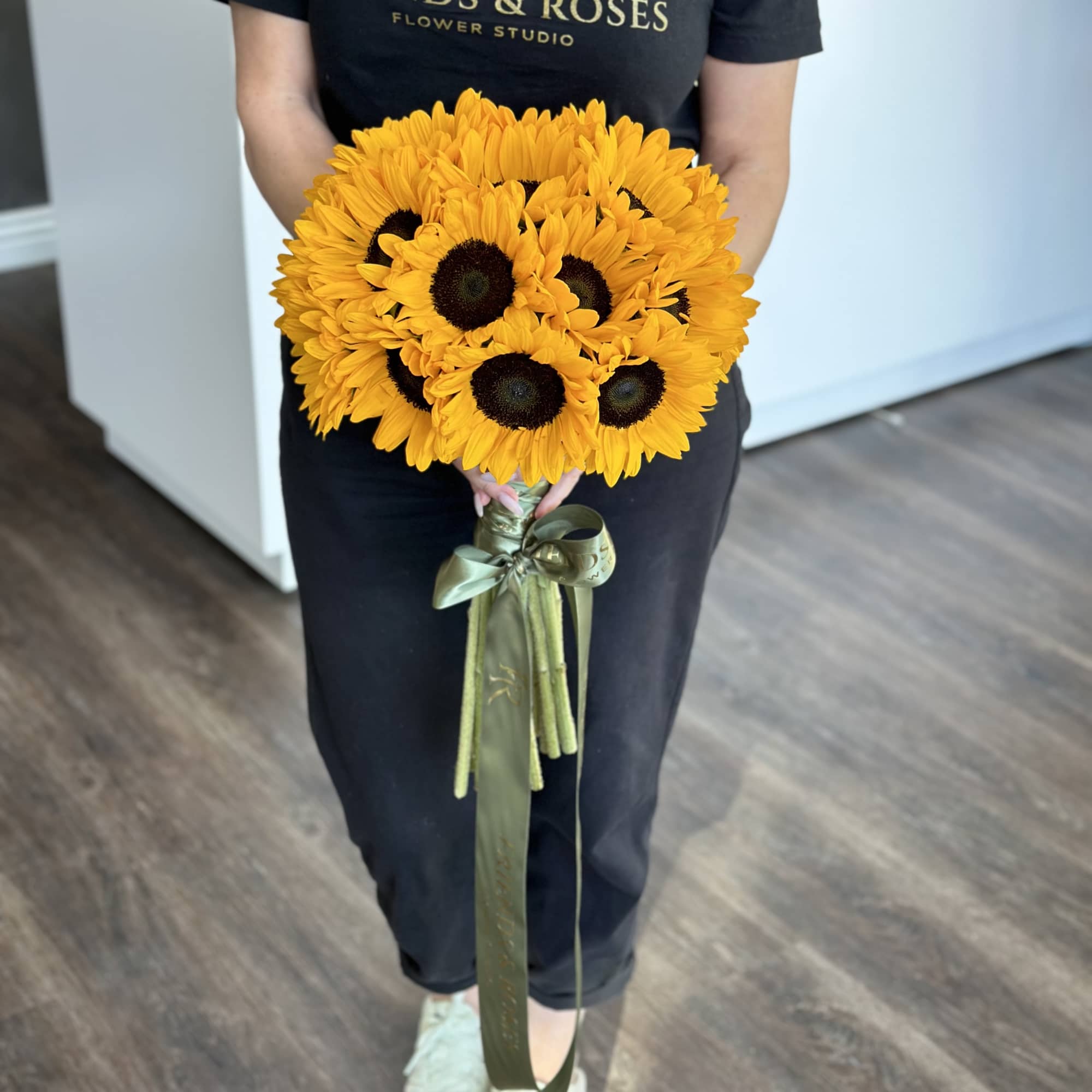 Person holding a bouquet of yellow sunflowers with a green ribbon