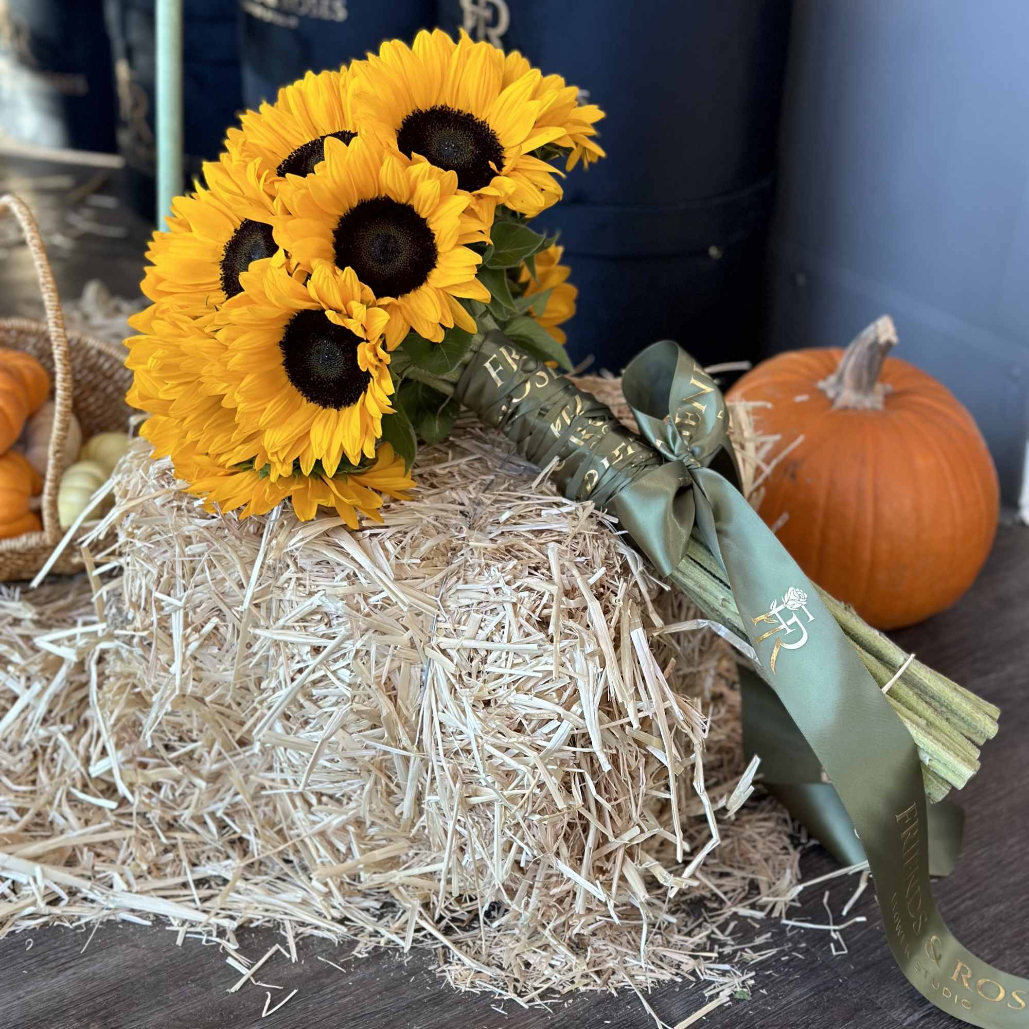 Bouquet of yellow sunflowers tied with a green ribbon beside pumpkins.