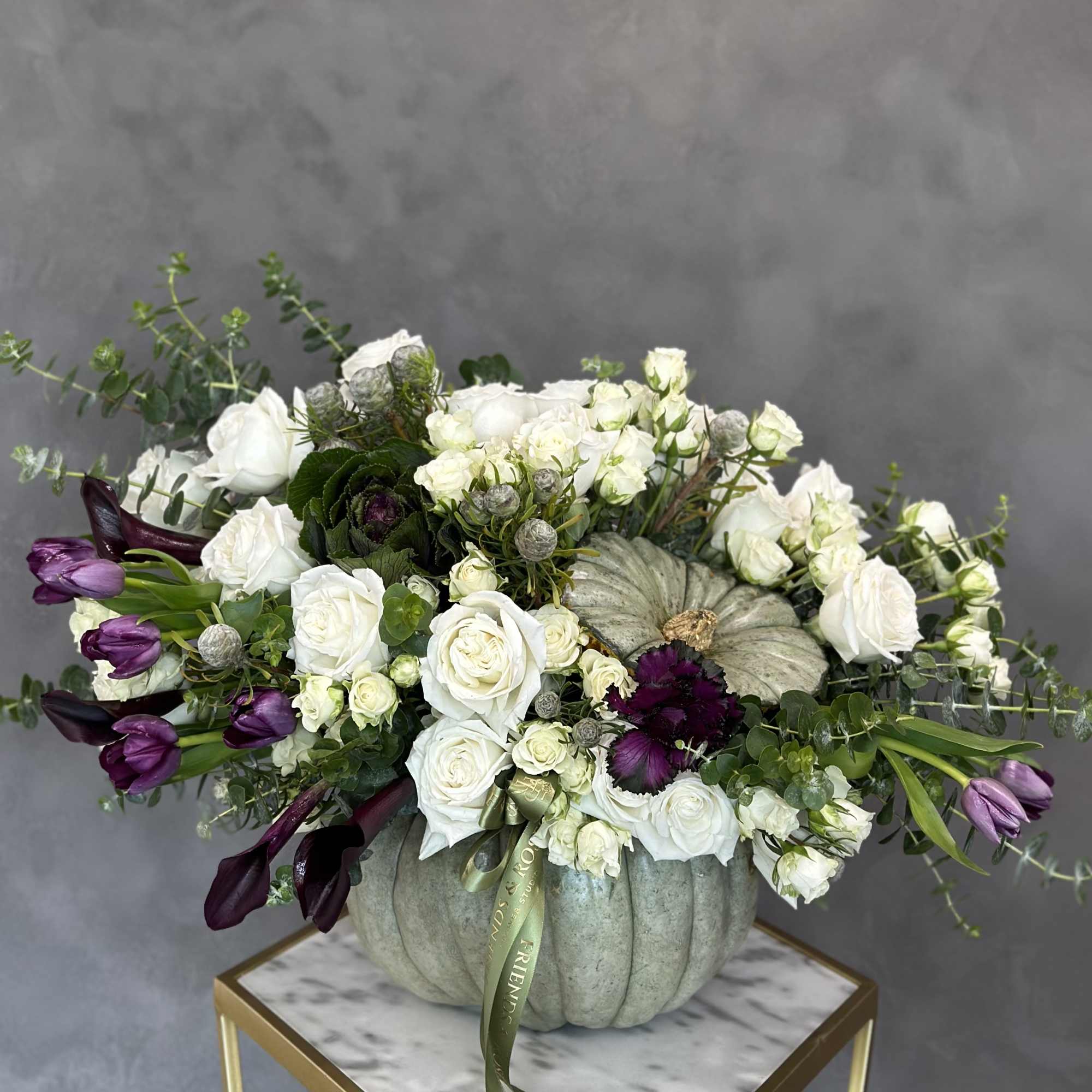 White roses and purple tulips arranged in a pumpkin vase