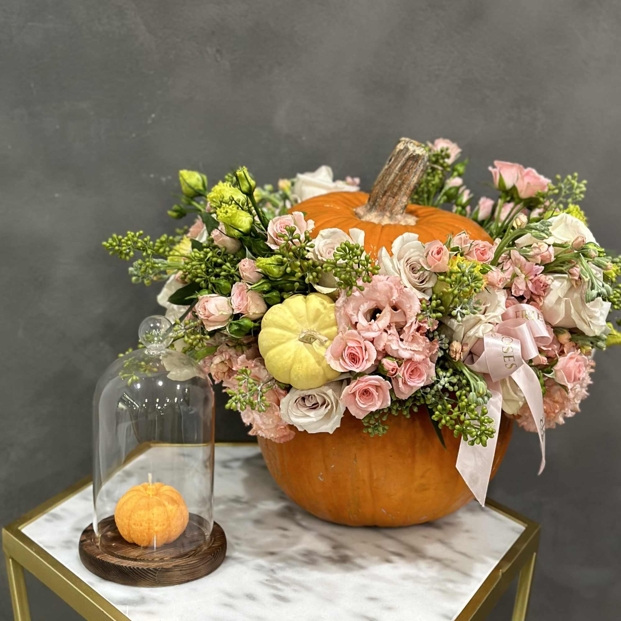 Floral arrangement in a pumpkin with pink and white blooms beside a glass cloche pumpkin display