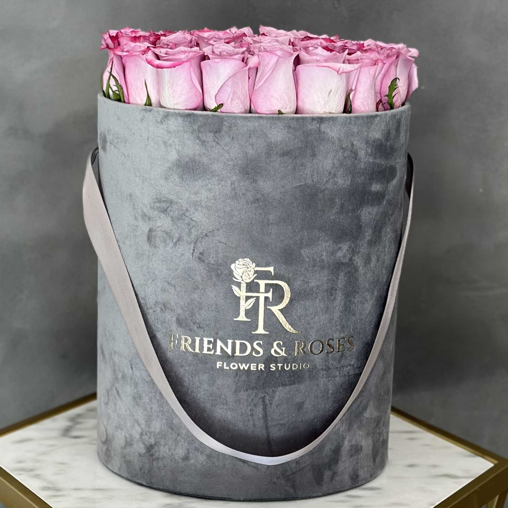 Pink roses arranged in a gray velvet hatbox with ribbon handles