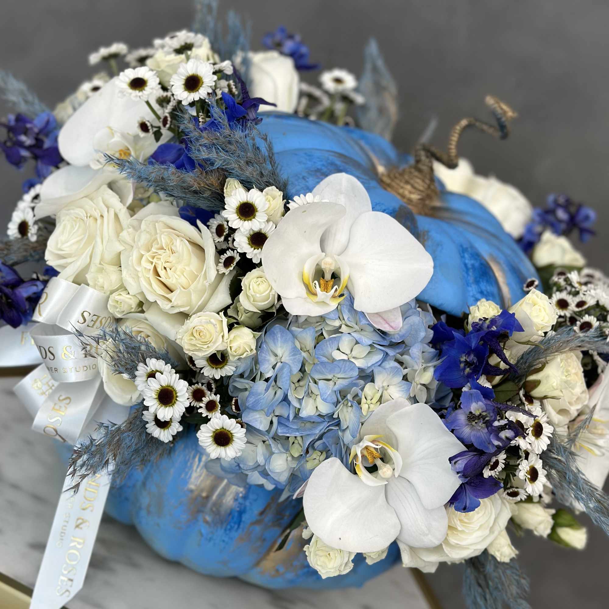Blue pumpkin centerpiece with white orchids, roses, and small daisies