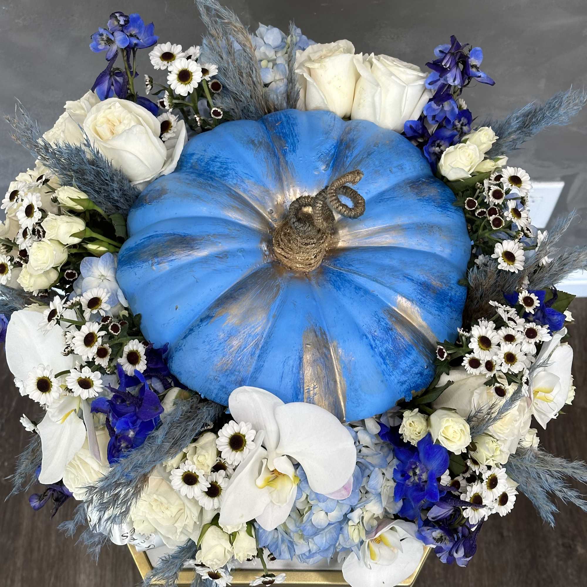 Blue pumpkin centerpiece surrounded by white and blue flowers