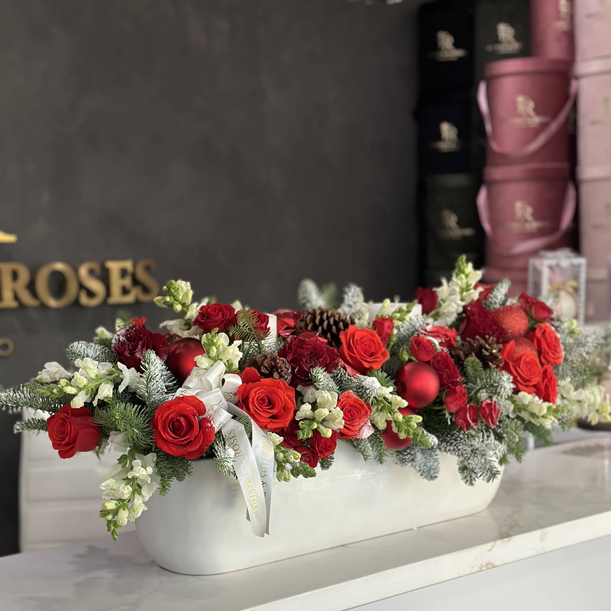 Long white planter filled with red roses, white flowers, and pinecones