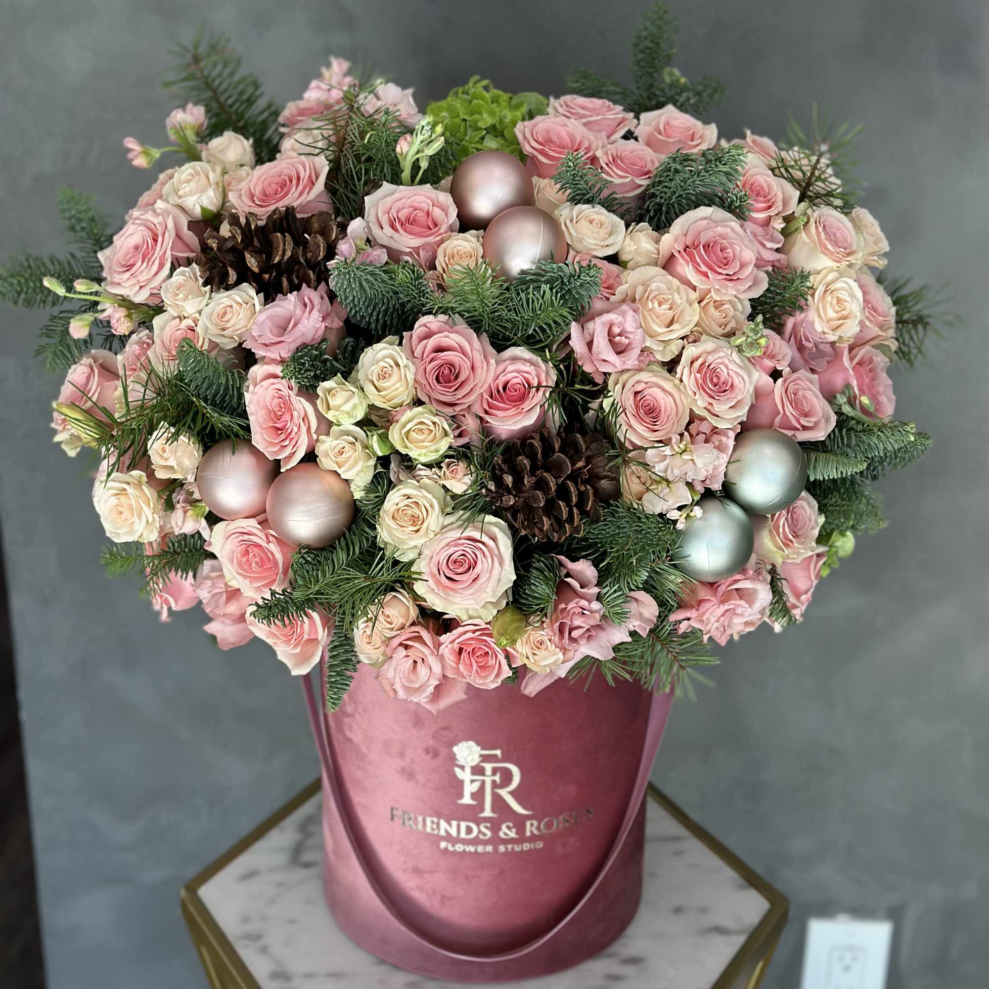 Pink and cream roses arranged in a round box with pinecones and ornaments