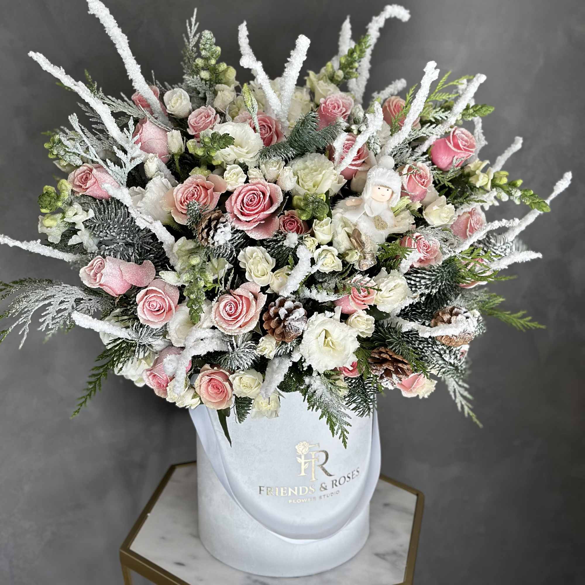Pink and white roses in a white hatbox with snowy accents